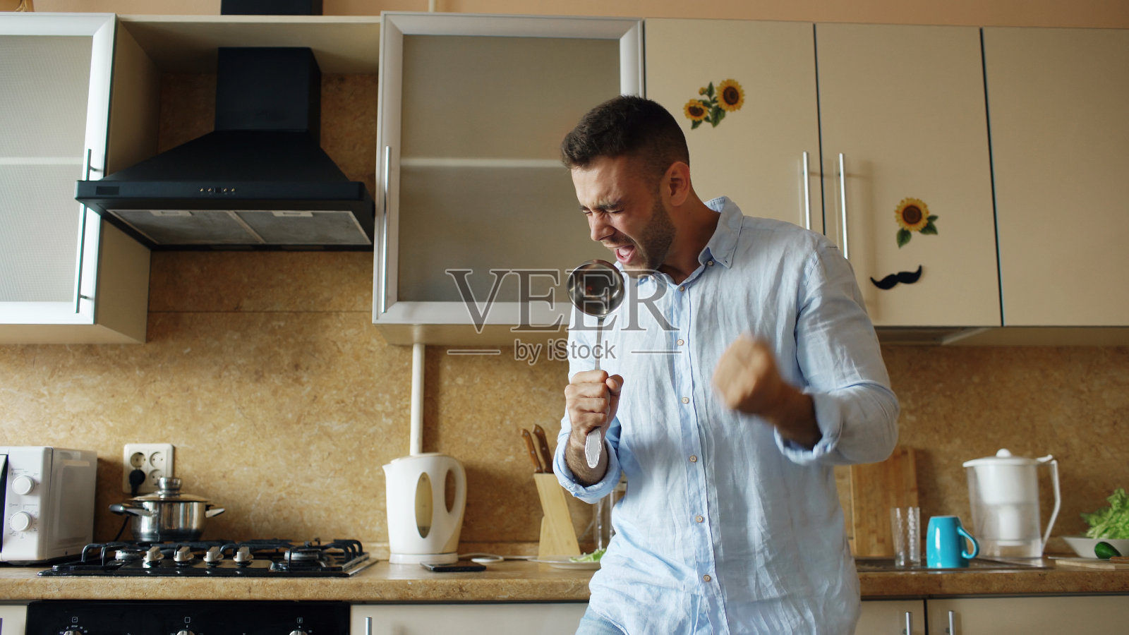 有吸引力的年轻有趣的男子跳舞和唱歌，同时在厨房做饭在家照片摄影图片