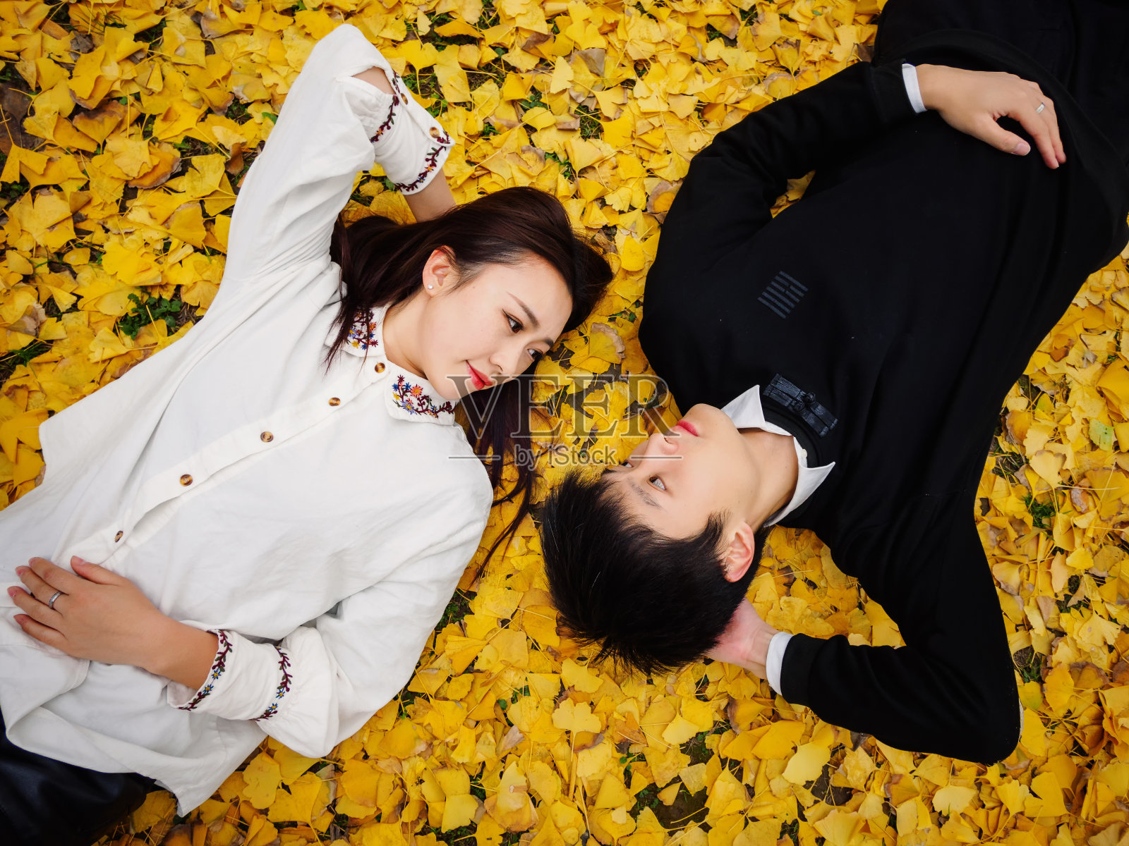 高角度观看一对中国年轻人躺在满是金黄银杏叶的秋日地面上，充满了爱情、情人的概念。照片摄影图片