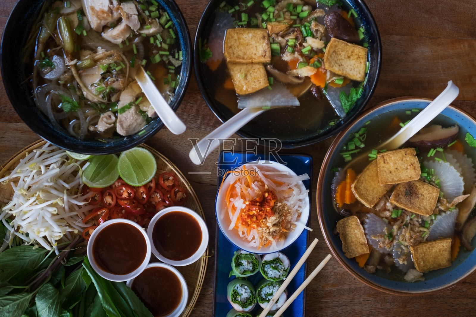 传统的越南菜。汤、面包卷和新鲜香草。木板表面上的盘子。照片摄影图片