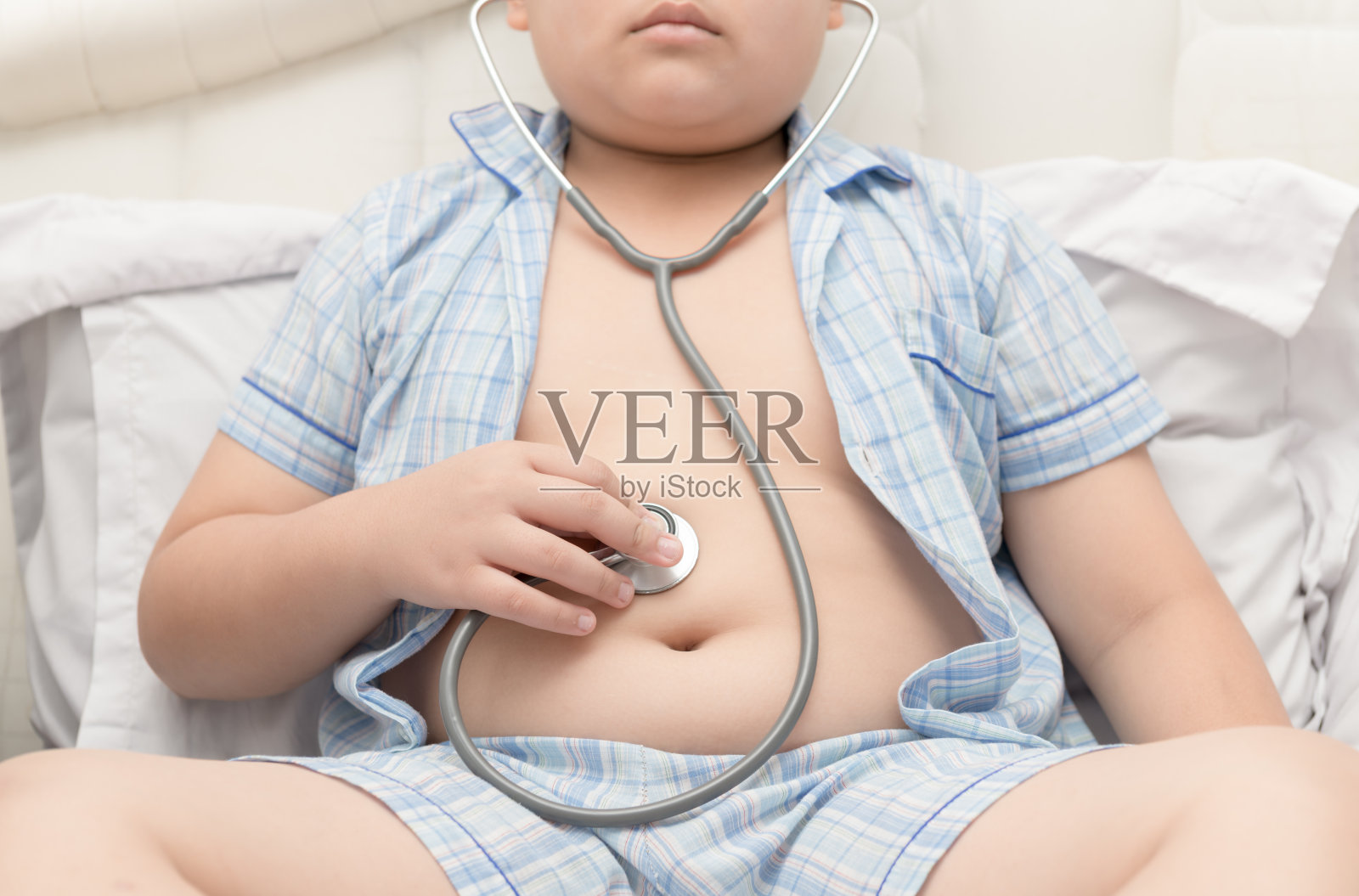 胖男孩用听诊器检查胃。照片摄影图片