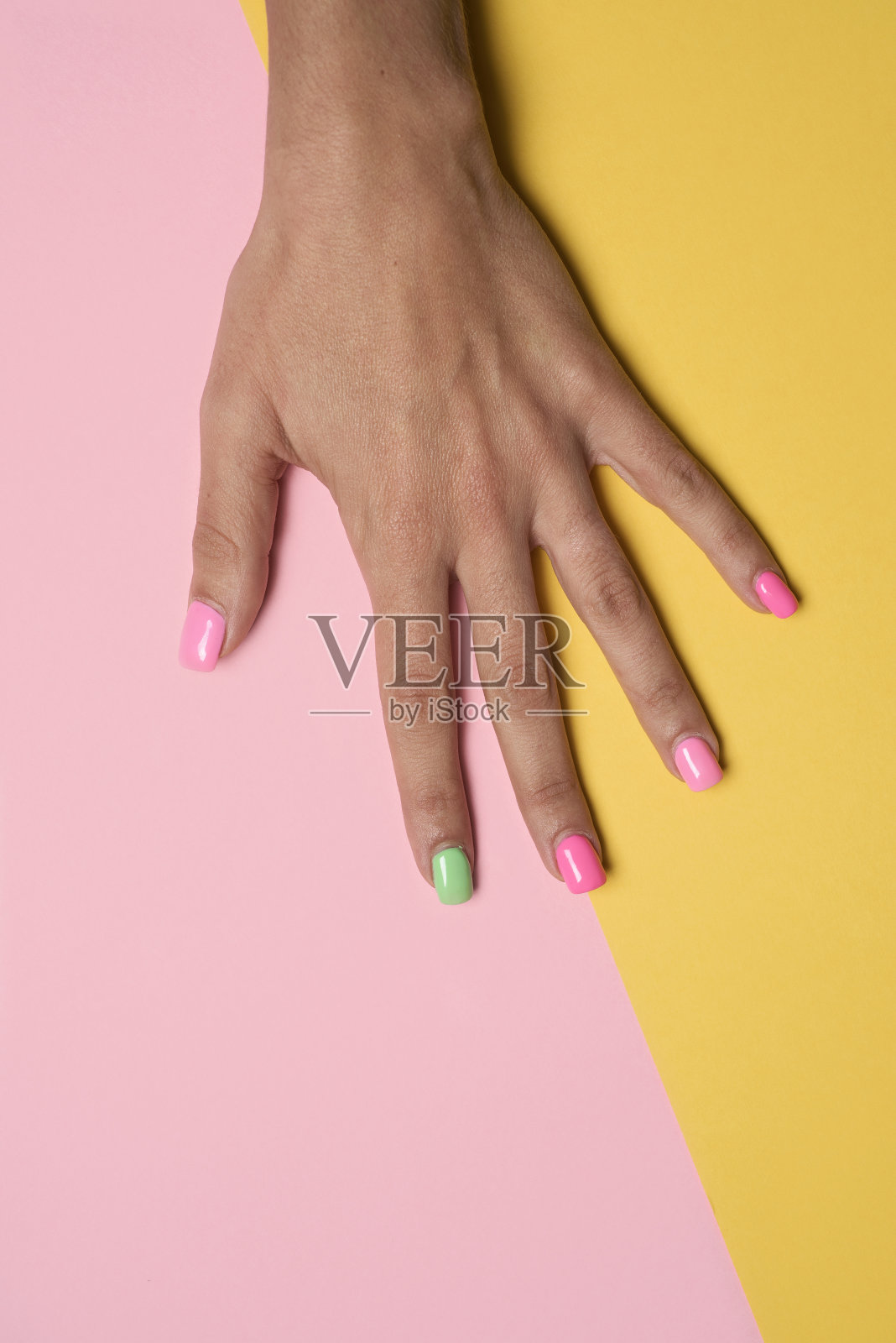 女人的手涂着粉红色和绿色的指甲照片摄影图片