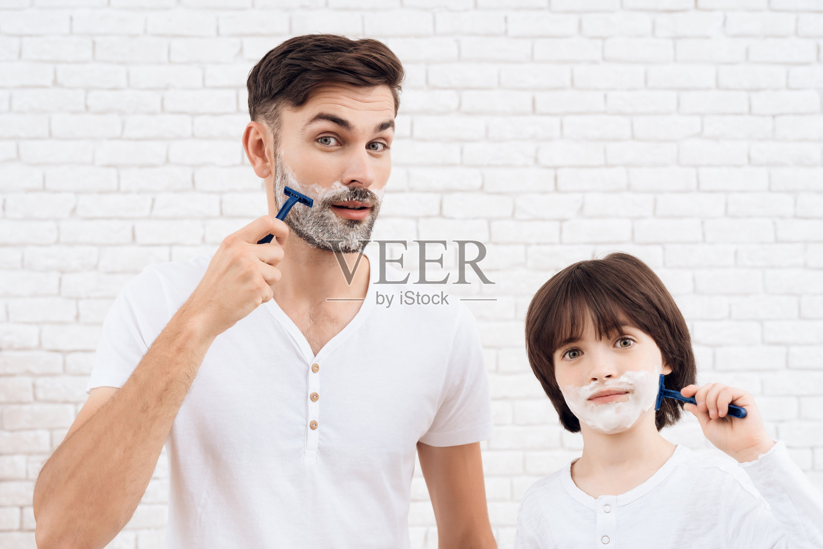 父亲和儿子花时间在一起。爸爸和儿子穿着一样的衣服。那个黑头发的小男孩学会了刮胡子。照片摄影图片