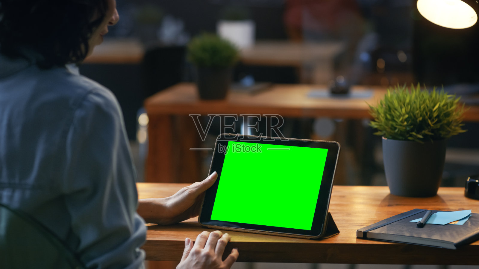 年轻女子坐在她的木制书桌前使用平板电脑模拟绿色屏幕，她使用各种滑动和触摸手势。照片摄影图片