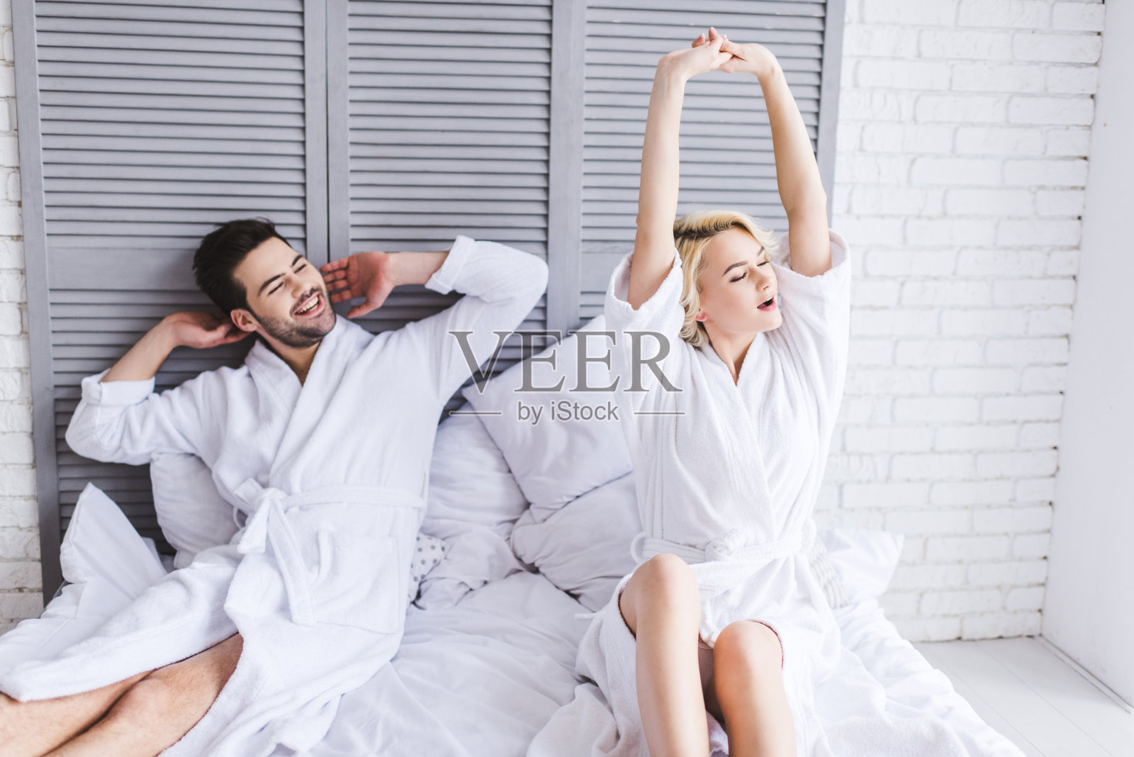 清晨，一对年轻夫妇穿着浴袍在床上伸懒腰照片摄影图片