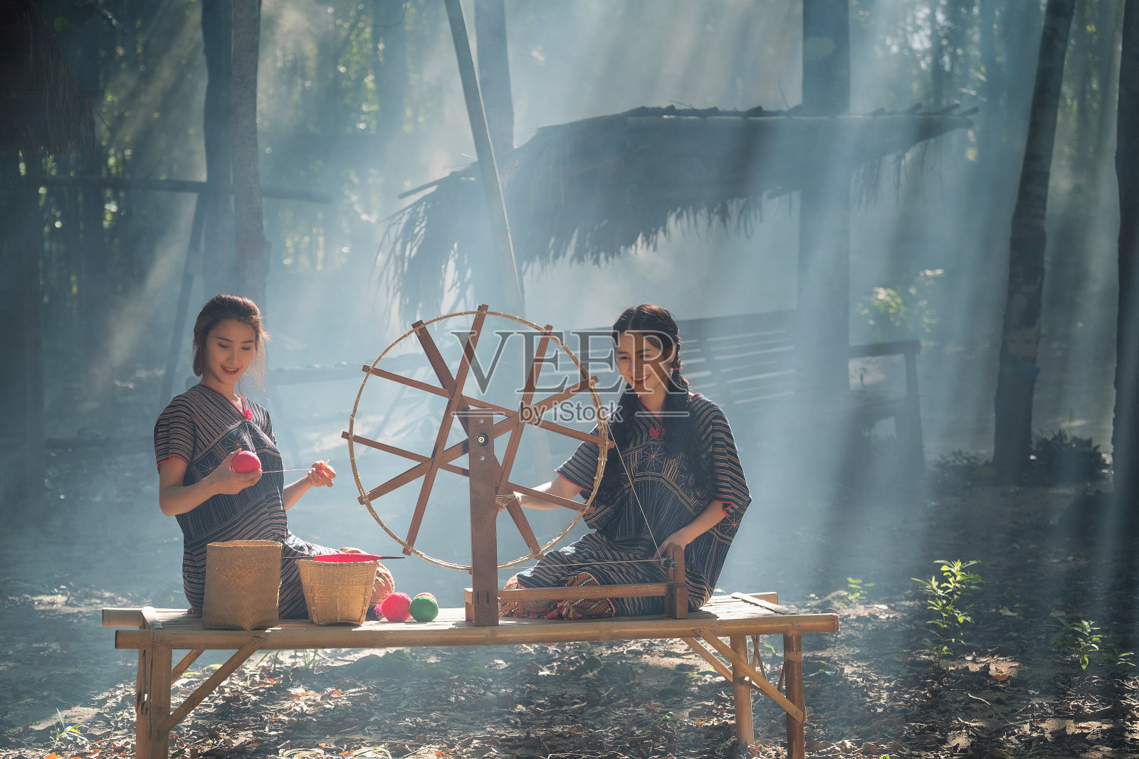 在泰国当地的一个森林自然村庄，两个美丽的泰国妇女微笑着在竹席上纺线照片摄影图片