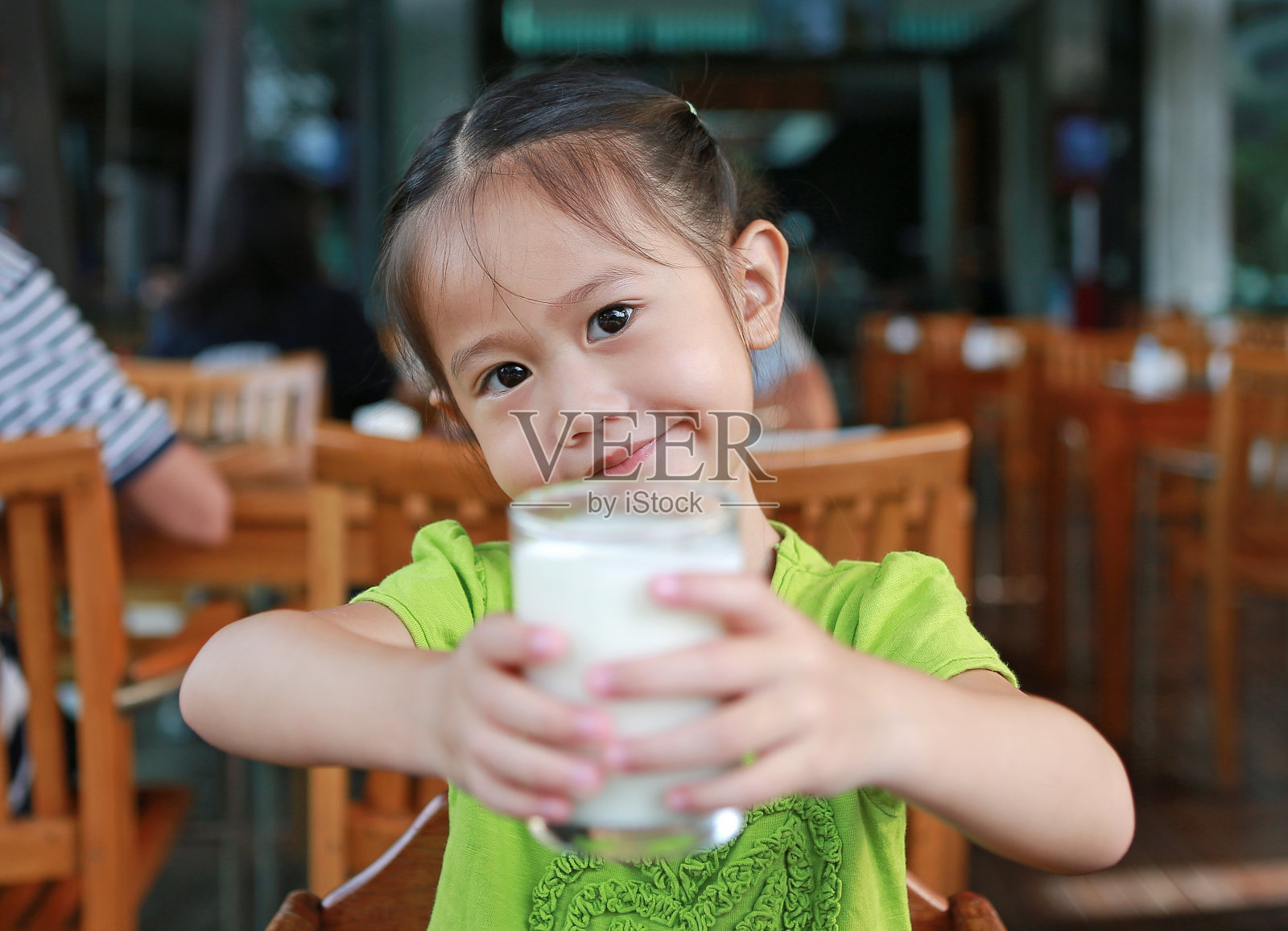 一个亚洲小女孩正在喝玻璃杯里的牛奶。照片摄影图片