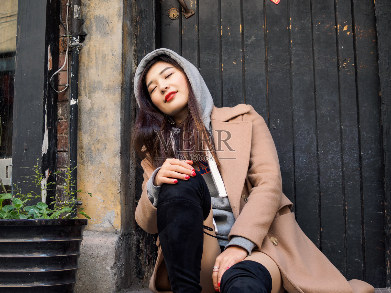 一个性感的中国年轻女孩坐在上海新天地的木门旁的肖像。照片摄影图片