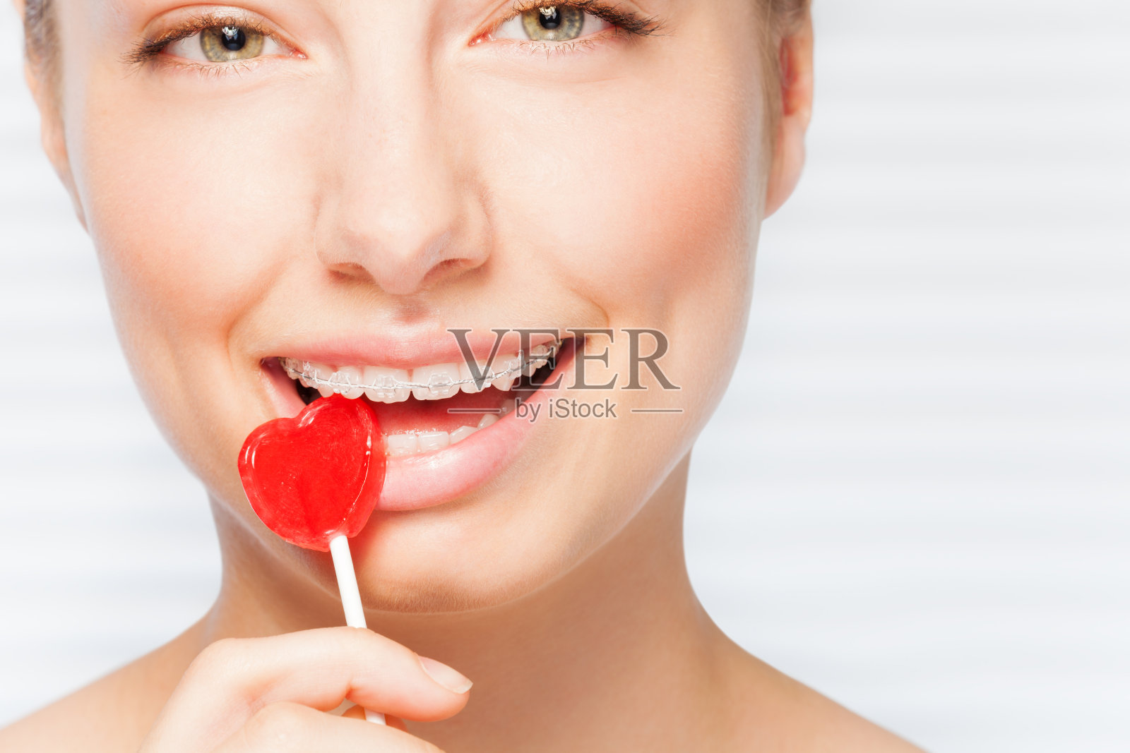 戴着牙套的女人咬着红色棒棒糖照片摄影图片