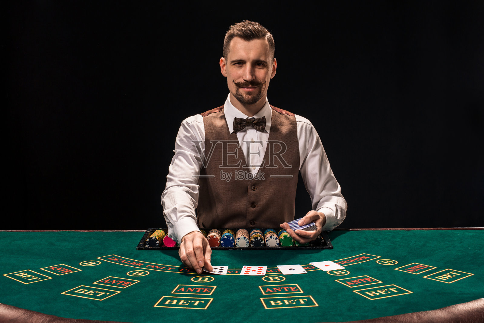 肖像的赌场老板正拿着扑克牌，桌上放着筹码。黑色背景照片摄影图片