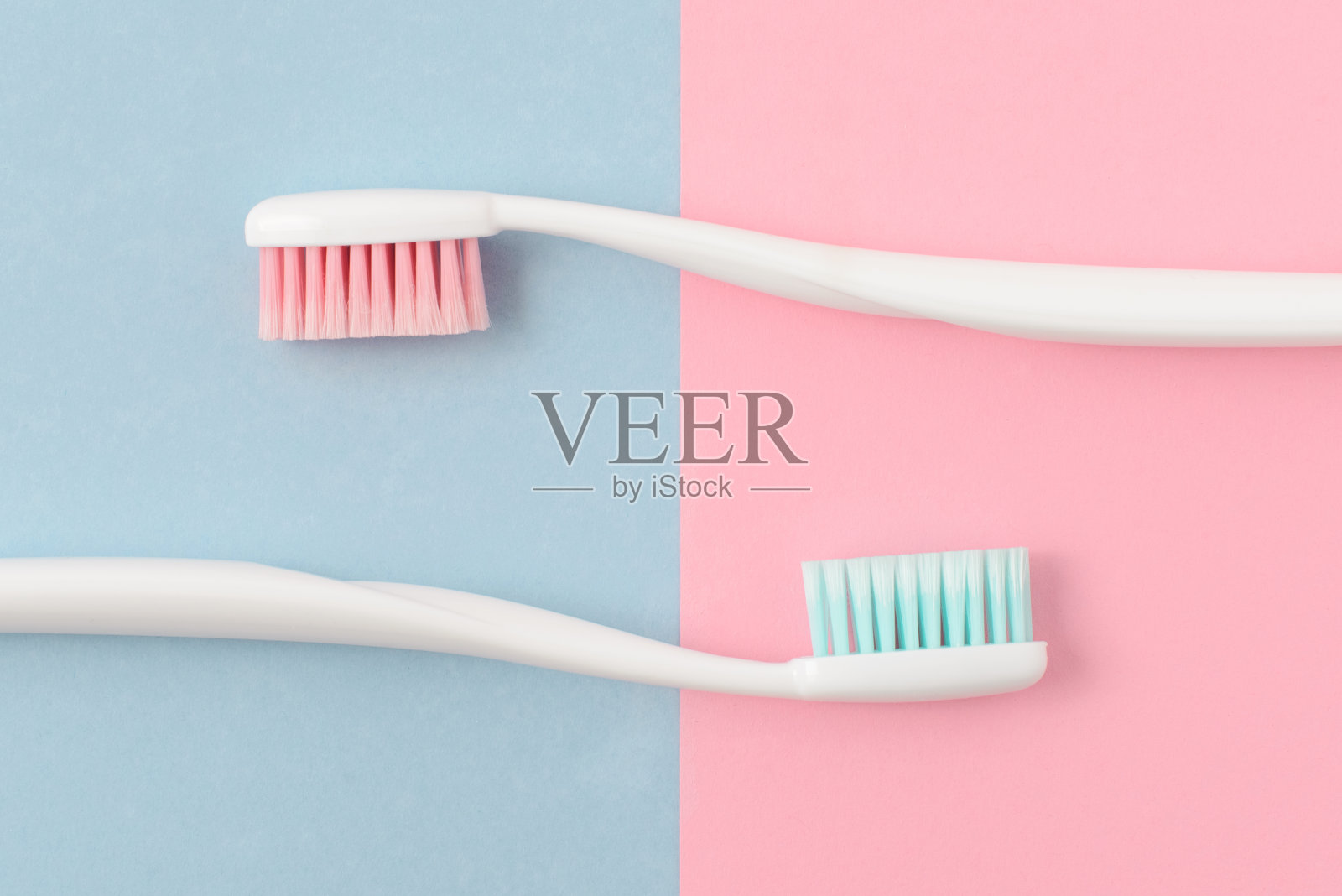 两个塑料白色牙刷的特写，粉红色和蓝色的鬃毛在粉红色和蓝色的背景。免费空间。照片摄影图片