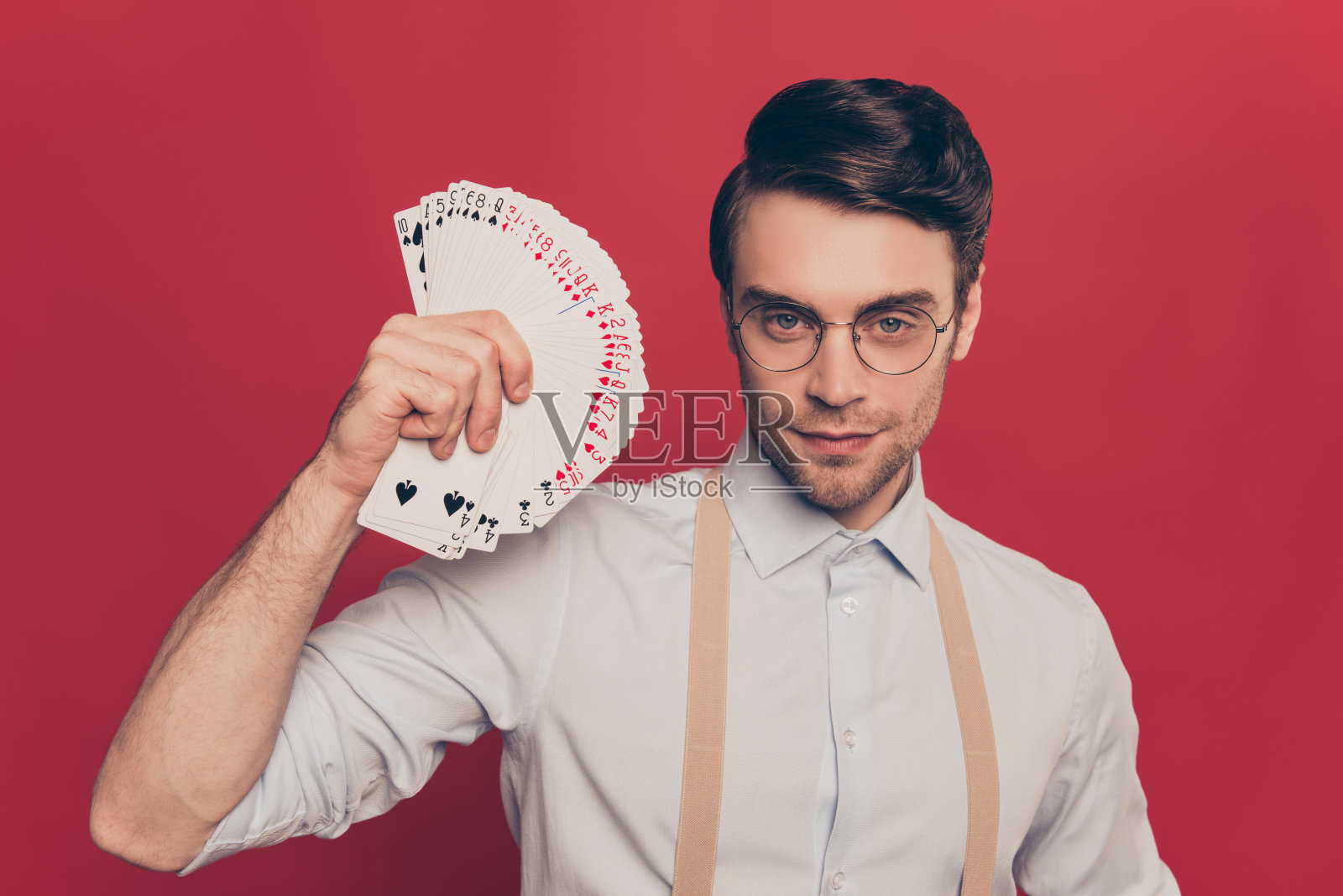 专业的，狡猾的魔术师，魔术师，赌徒在休闲装，眼镜，手持，显示套甲板的卡近面，站在红色的背景照片摄影图片