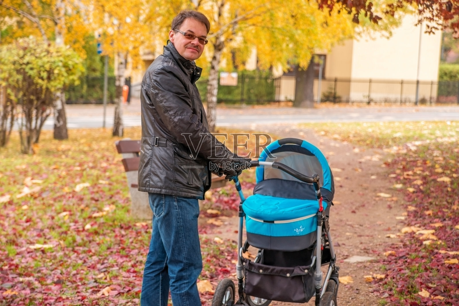 在公园里推着婴儿车散步。老爸推着婴儿车。照片摄影图片