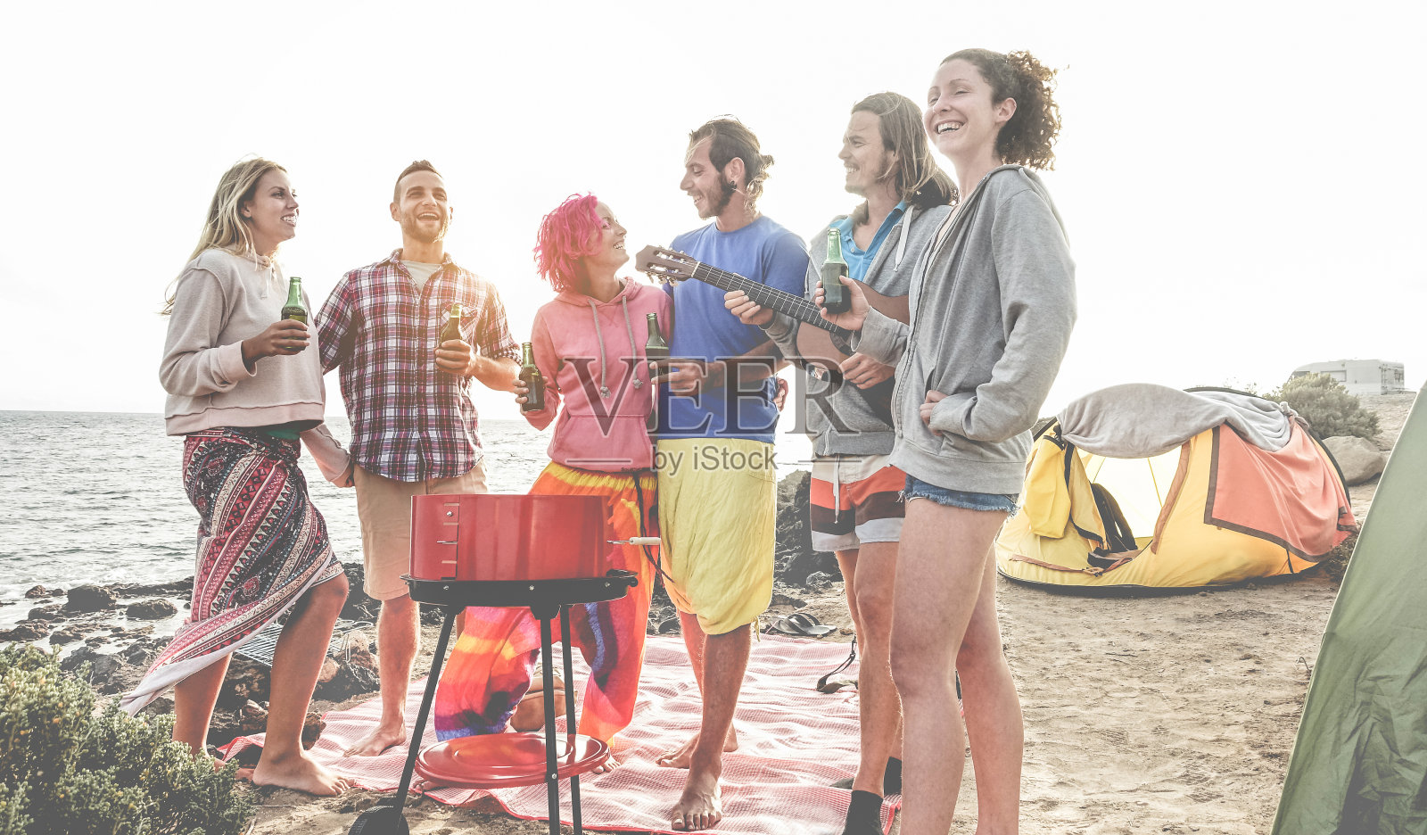 快乐的朋友喝啤酒在露营烧烤野餐旁边的海洋-冲浪者有乐趣和一起欢笑在夏季聚会假期-旅游，假期和友谊的概念照片摄影图片