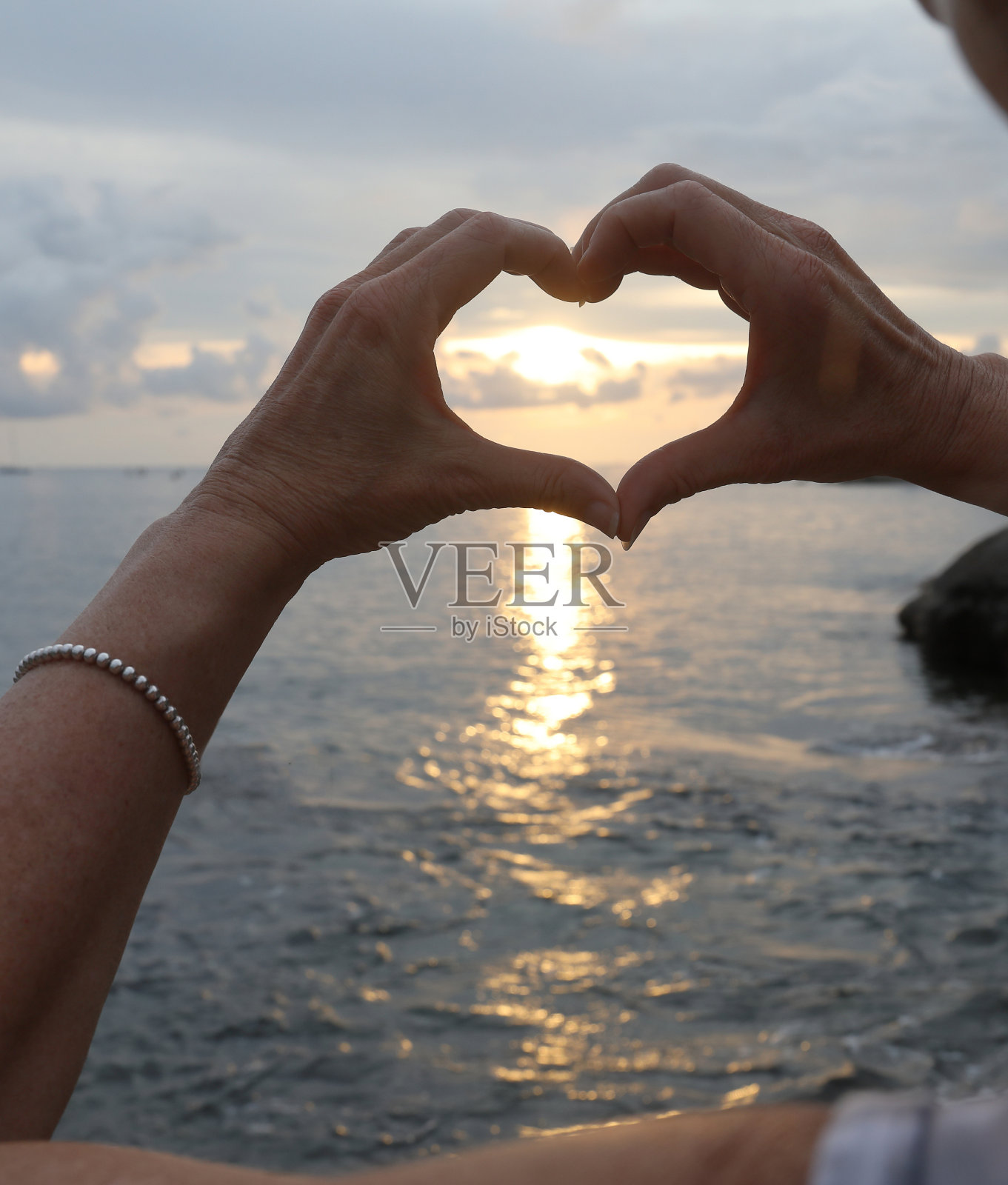 手在夕阳和大海的映衬下形成一颗心照片摄影图片