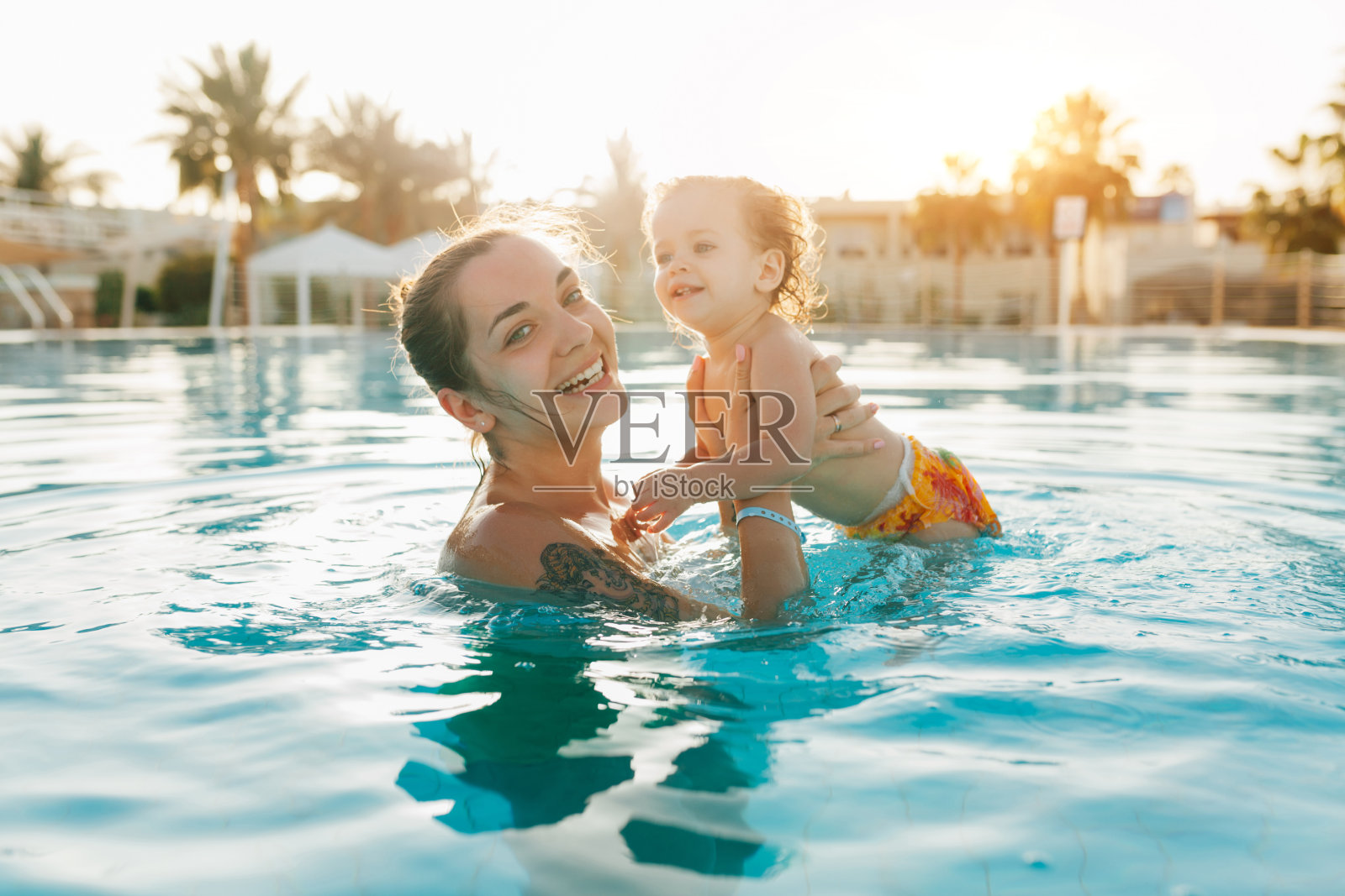 母亲抱着孩子在热带夏季游泳池背景照片摄影图片