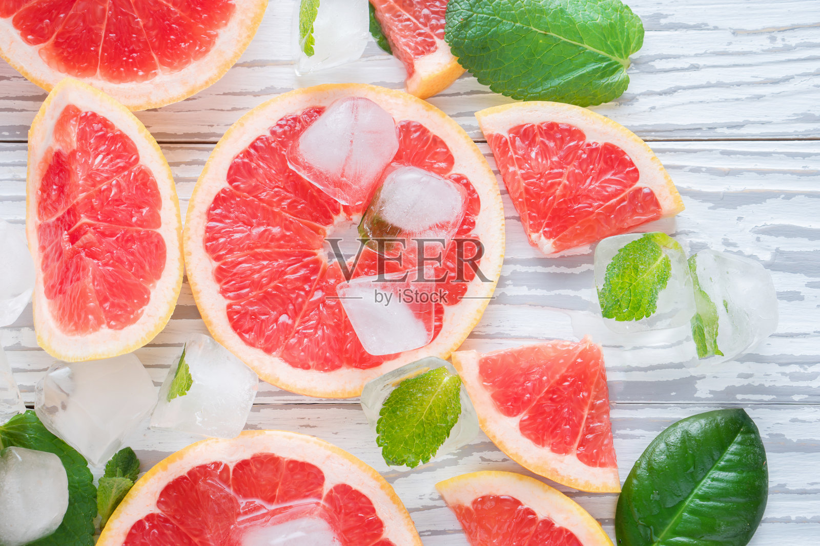 俯视图红色柚子片，冰和薄荷在一个白色的木制背景。健康饮食的概念。排毒。照片摄影图片