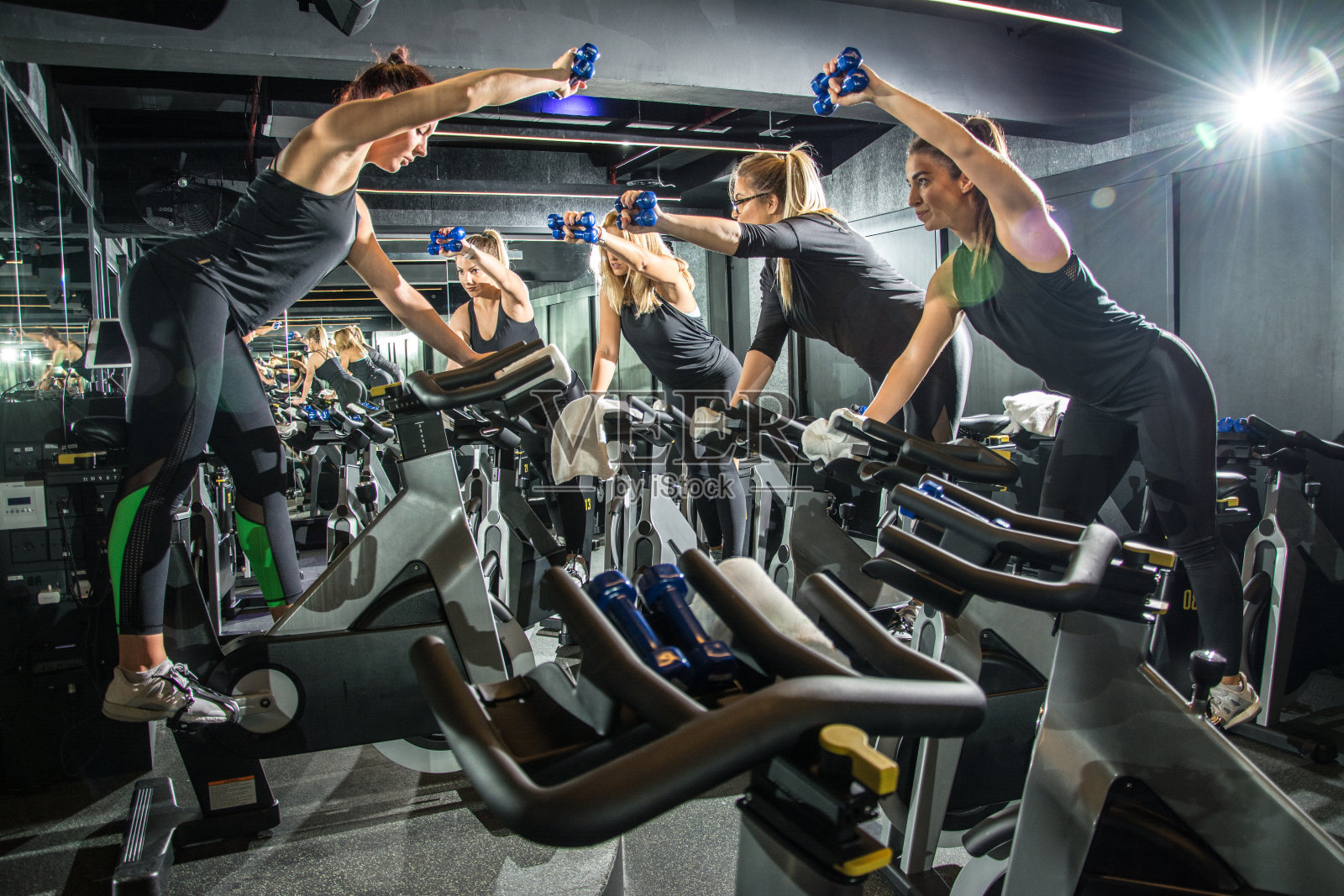 一群运动女友一起在健身房的自行车课上用哑铃训练。照片摄影图片