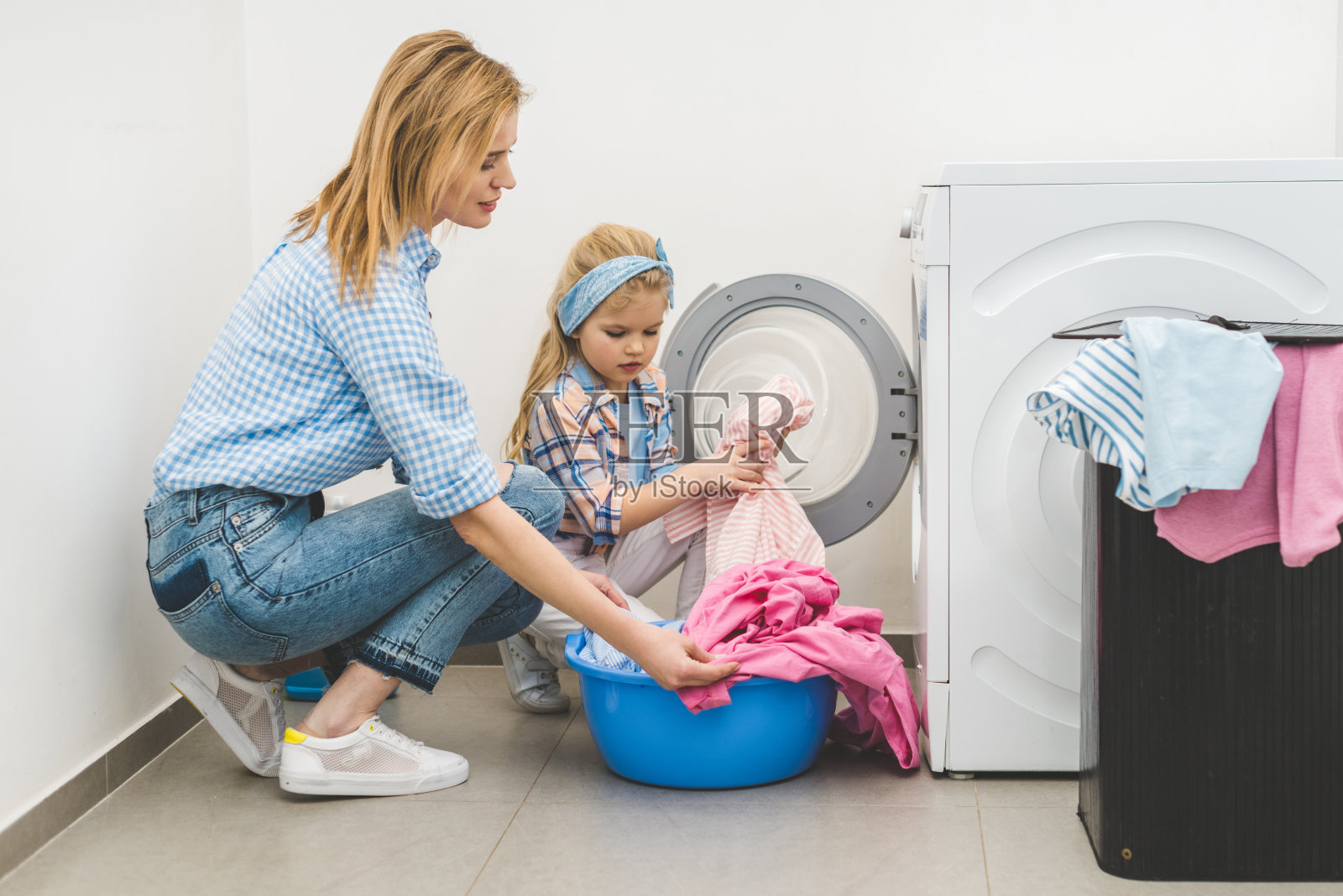 母亲和女儿在家里把衣服放进洗衣机的侧视图照片摄影图片