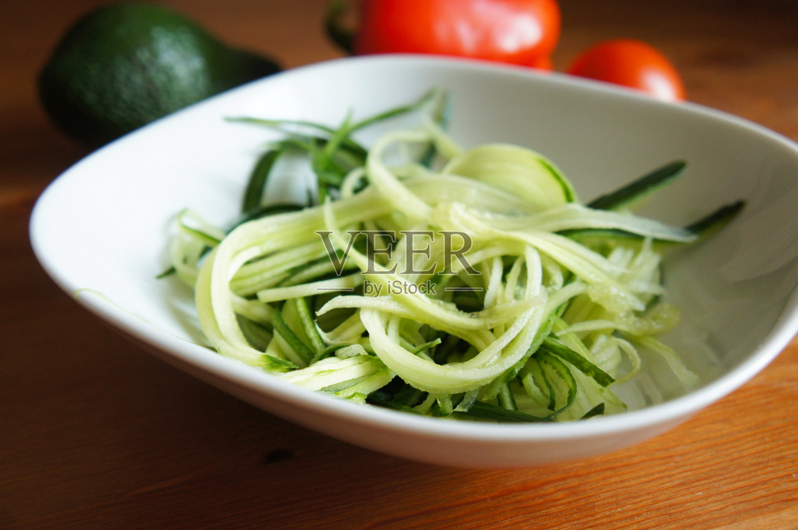 白碗里的生黄瓜绿意面和木桌上的蔬菜照片摄影图片