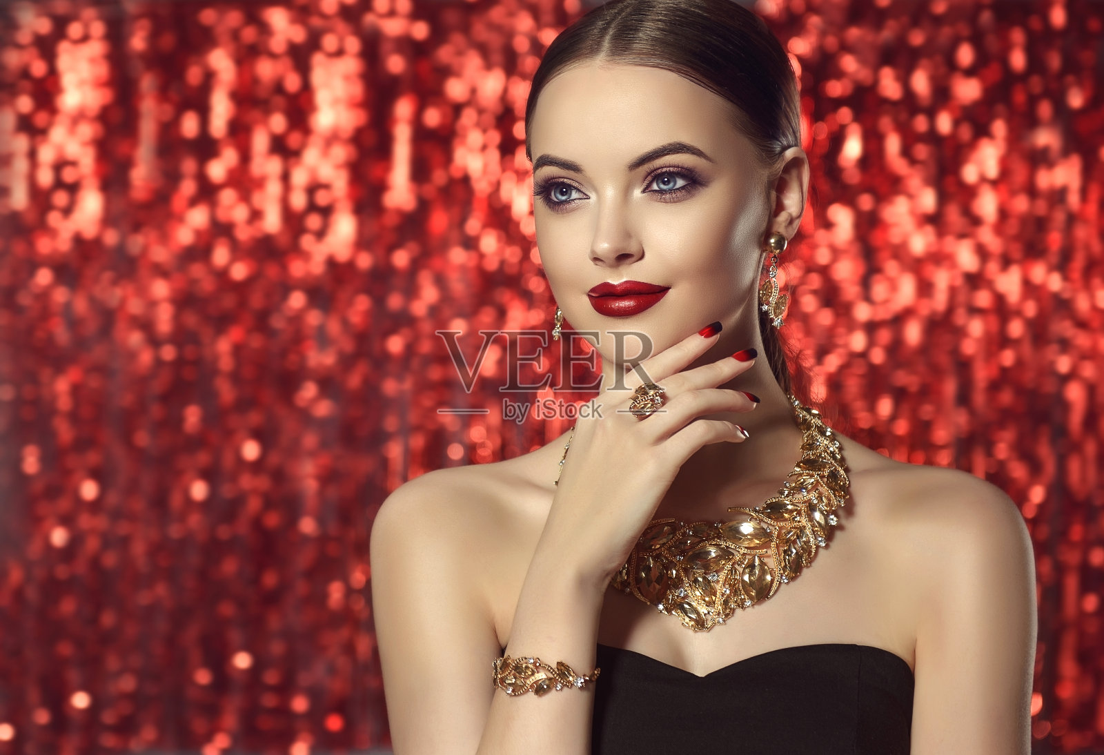 美丽的女人正在展示镀金珠宝和完美的化妆。照片摄影图片