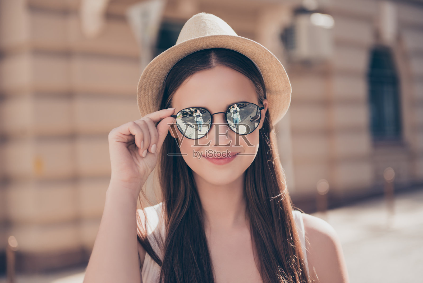 年轻可爱的微笑女孩在镜子太阳镜和帽子在假期，在城市户外散步的特写。她很高兴，正在修她的眼镜照片摄影图片