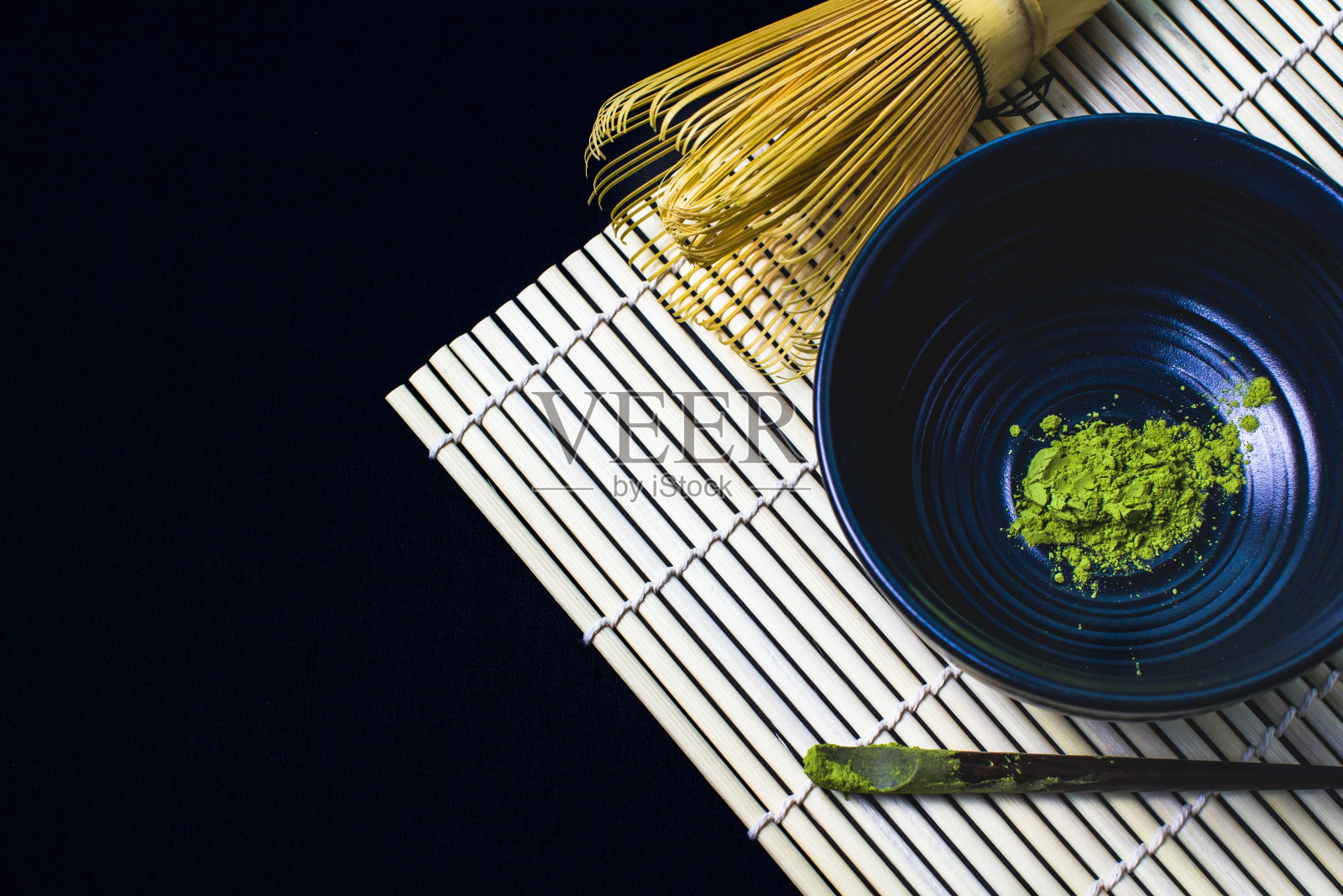 把竹打蛋器和抹茶绿茶粉放在黑色的背景上。照片摄影图片