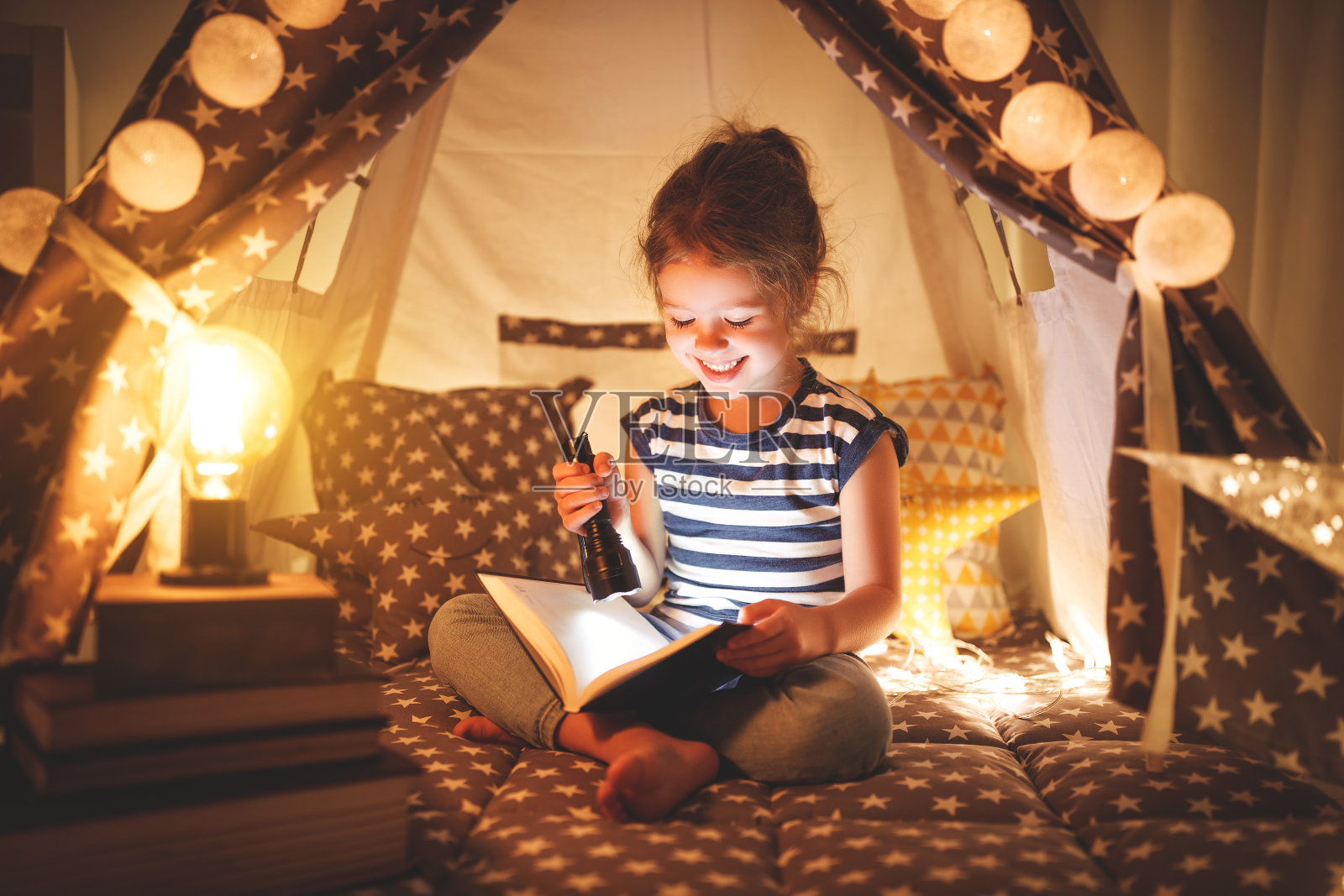 快乐的小女孩在家里的帐篷里笑着看书照片摄影图片