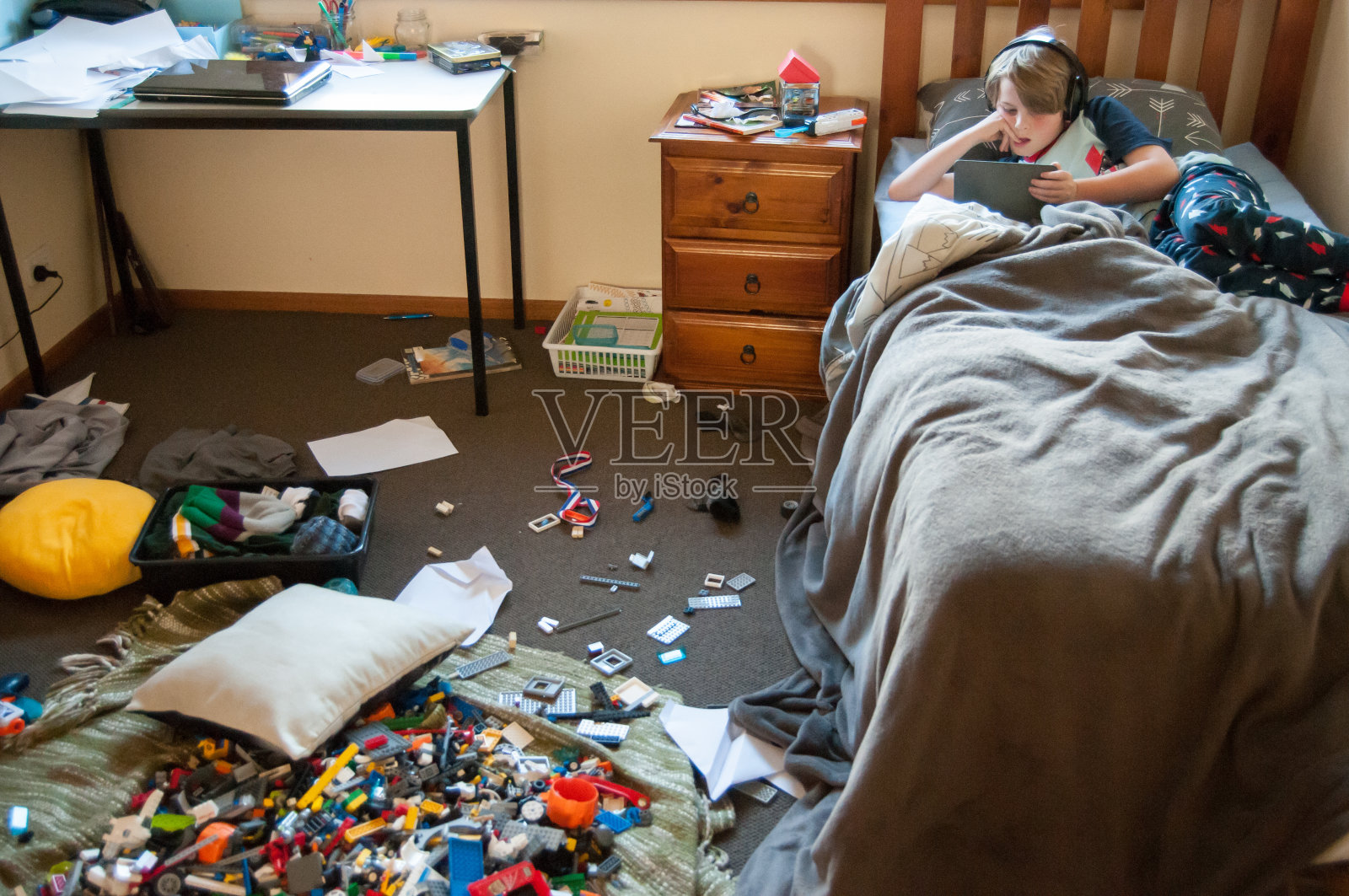 孩子躺在床上的电子设备和一个非常凌乱的房间照片摄影图片