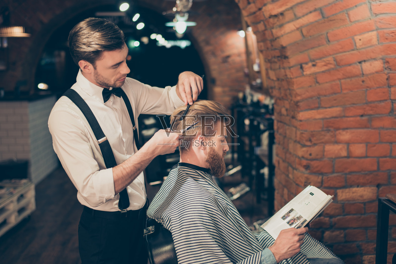 一个留着红胡子的家伙正在一家理发店里看杂志，同时还在给一位打扮优雅的造型师剪一个新发型。都是忙碌照片摄影图片