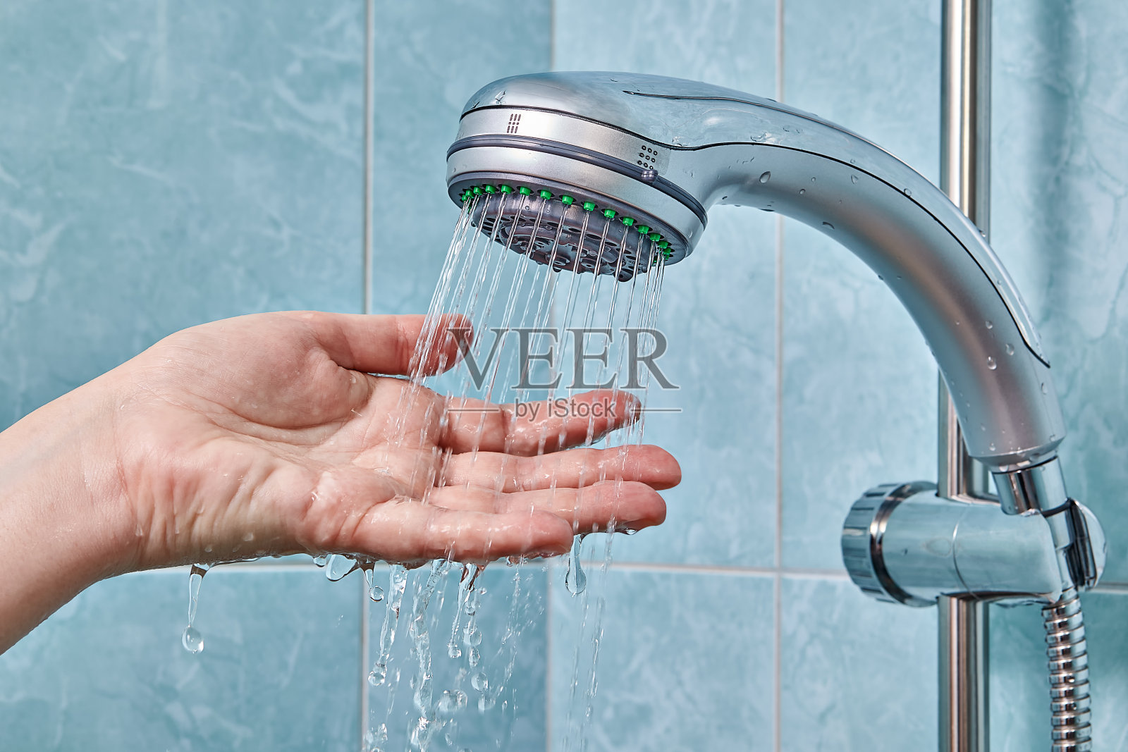 软管夹住淋浴器，用手检查水温。照片摄影图片