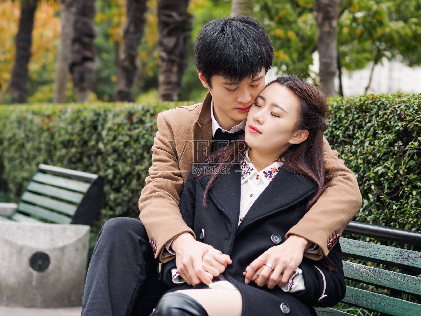 一对中国年轻人坐在长椅上的肖像秋天公园，手牵手拥抱在一起，情人的概念。照片摄影图片