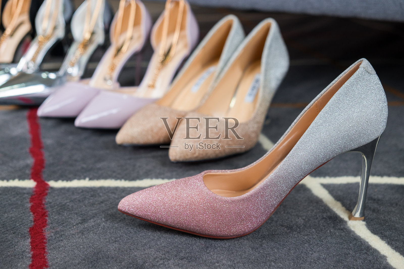 灰色地毯上穿着银色和粉色的女式高跟鞋。时尚性感的配件。照片摄影图片