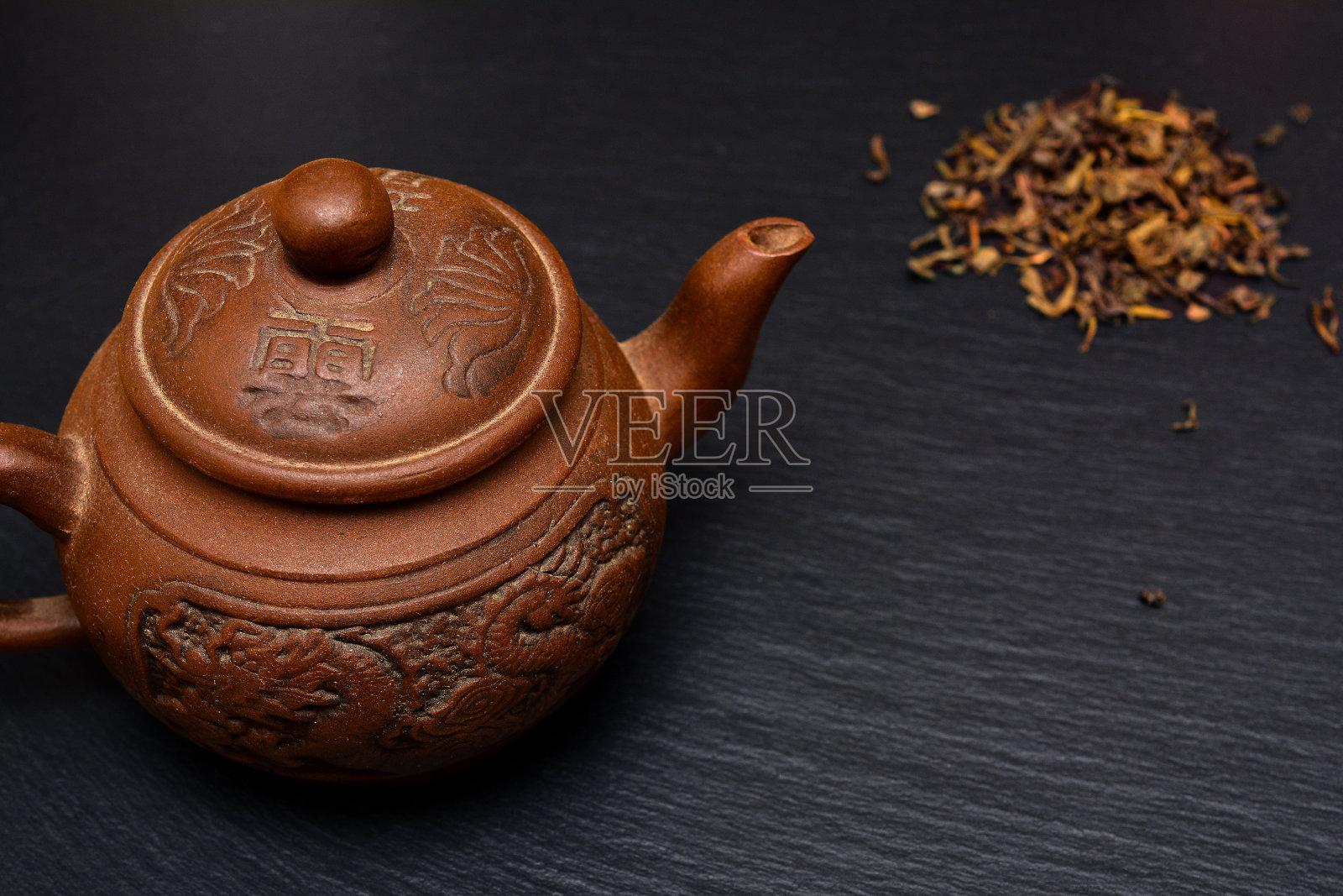 茶壶和干茶叶在黑色石板板，盘子或托盘。照片摄影图片