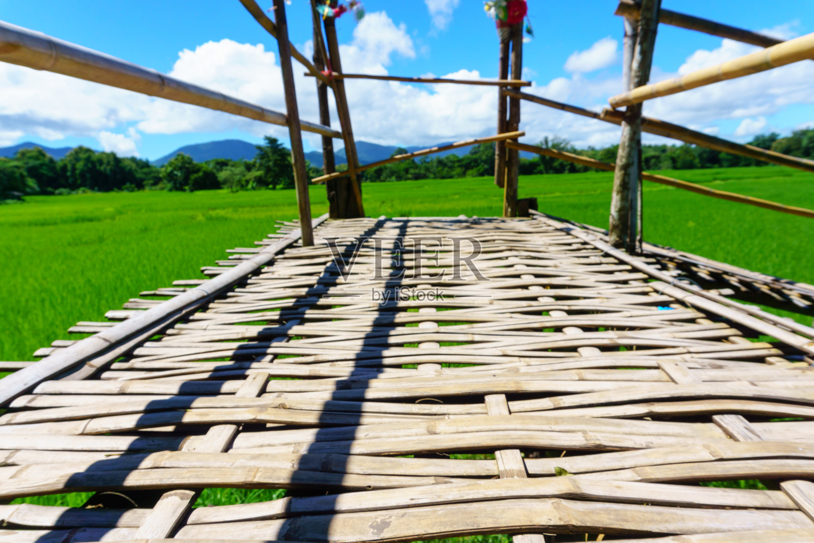 在乡村阳光明媚的日子里，乡村竹桥通往稻田的小路与蓝天和蓬松的云紧密相连。南邦，泰国北部。桥名“Sapan Boon Wat Pa That San Don”照片摄影图片
