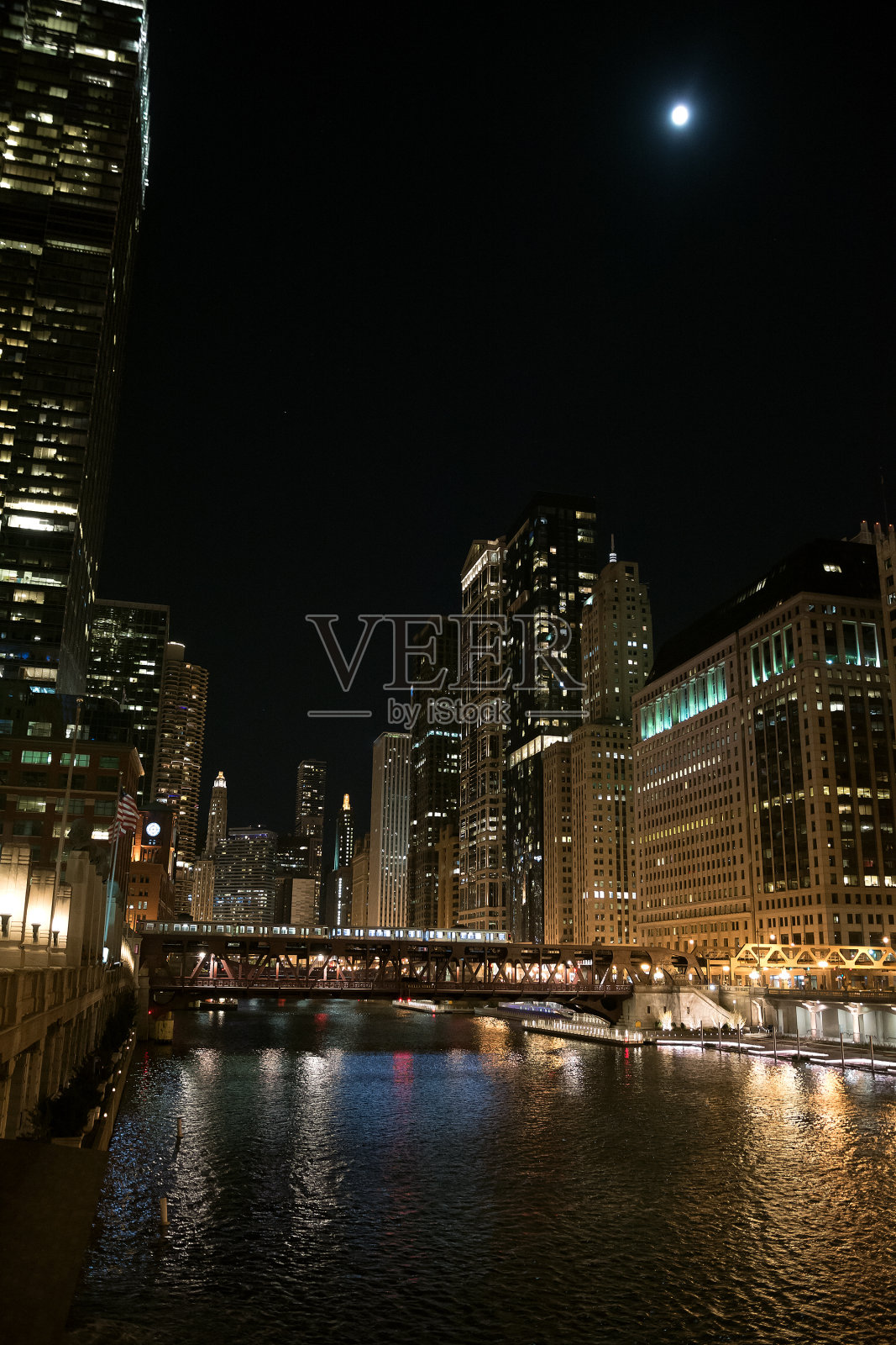 芝加哥的河滨步行街在夜晚有古老的吊桥，照亮了城市市中心的建筑和月亮。照片摄影图片