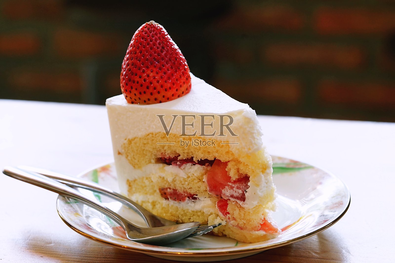 草莓酥饼上面有一个大的新鲜草莓放在白色盘子和咖啡馆环境的木桌上。维多利亚海绵蛋糕。照片摄影图片