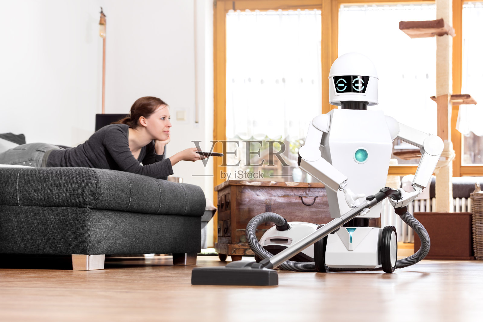 当一个机器人在做家务时，女人正在享受她的闲暇时光。阿艾正在用真空吸尘器清扫地板照片摄影图片