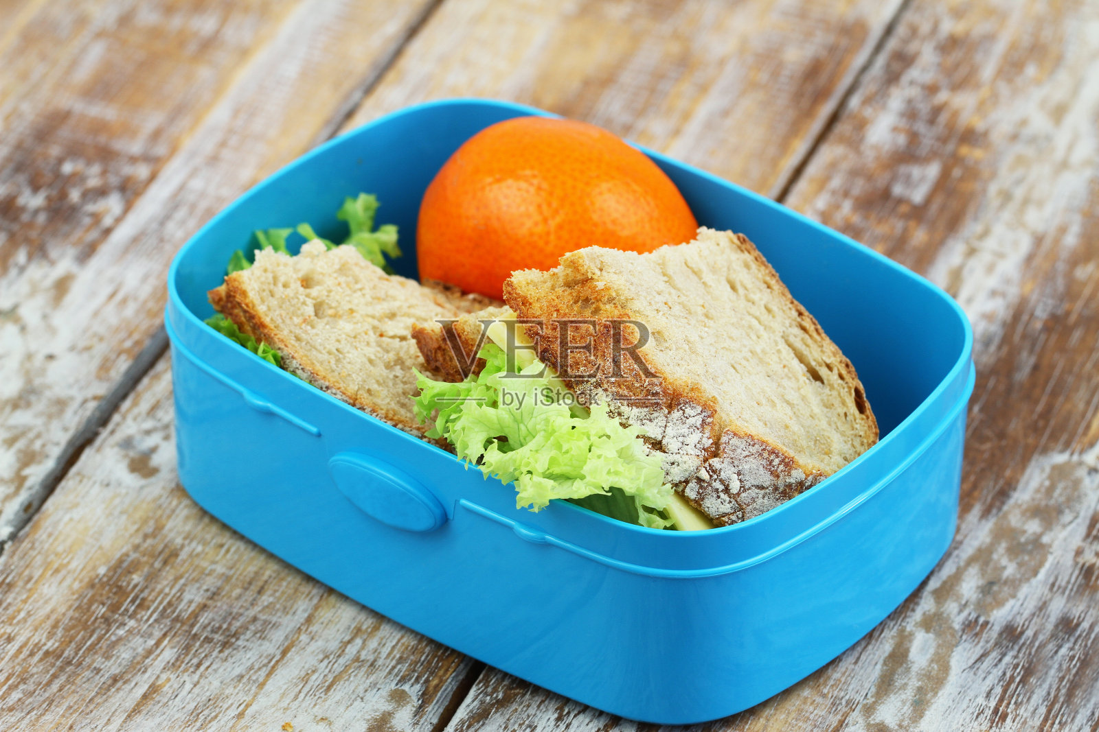 午餐盒里是带有奶酪和莴苣的乡村面包三明治，木头表面上是桔子照片摄影图片