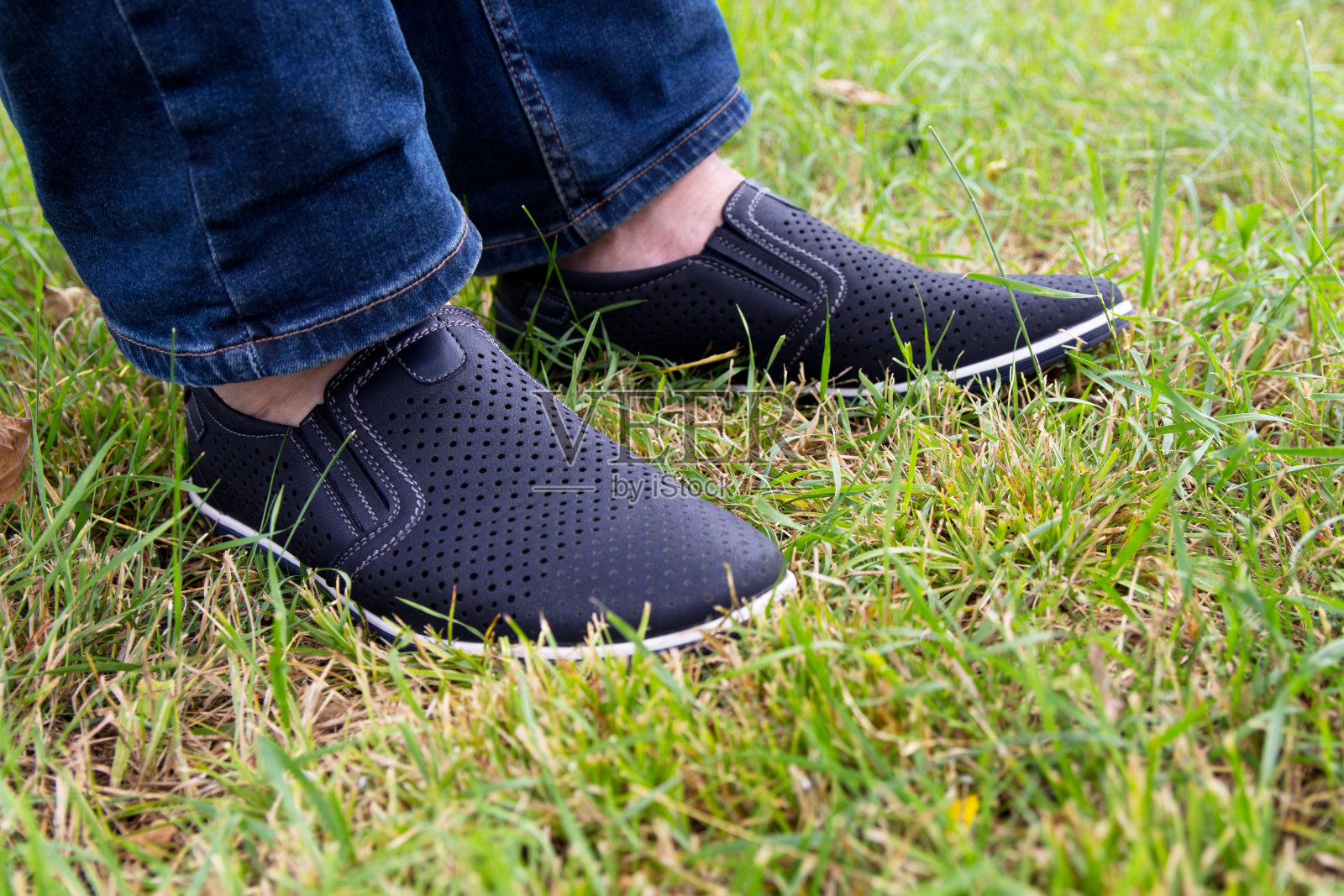 一个穿着牛仔裤和夏鞋的男人站在绿草的背景上。皮鞋。照片摄影图片