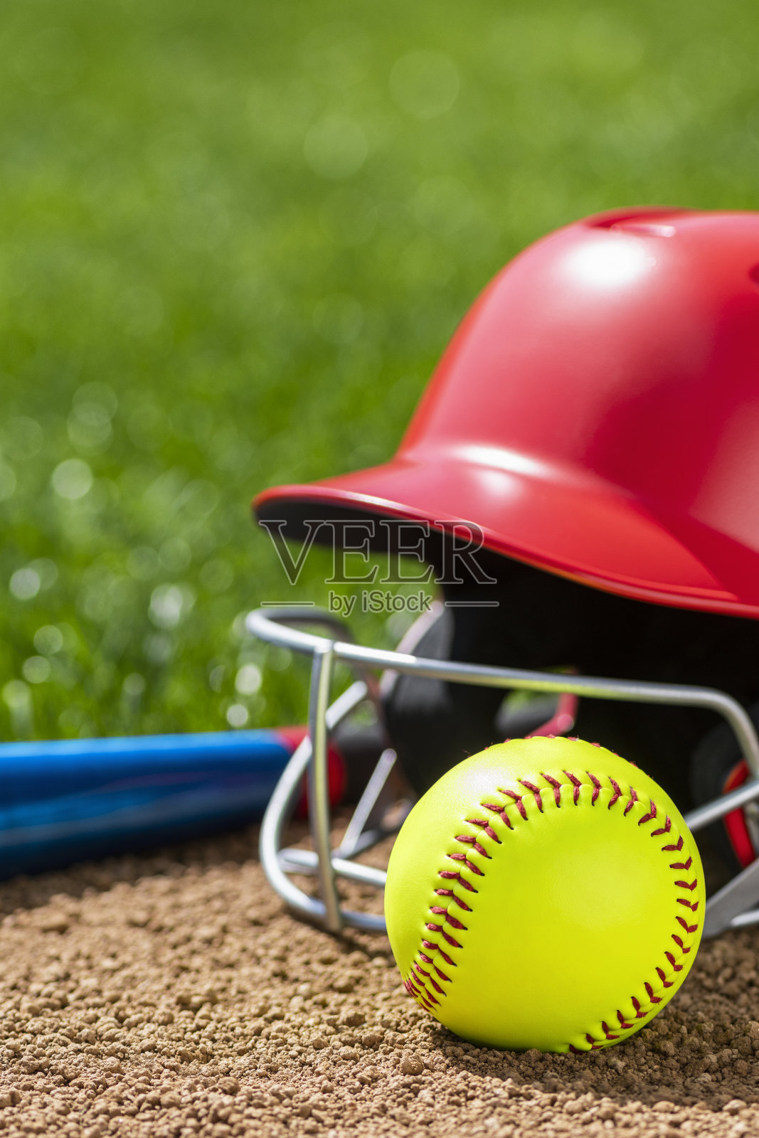 一个黄色垒球，红色的头盔和铝球棒放在泥土里照片摄影图片