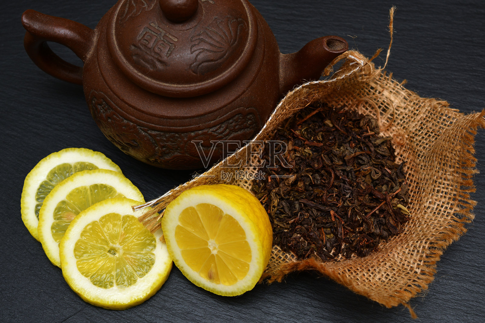 茶壶，熟透柠檬的一半和片，干茶叶放在黑板，盘子或托盘。照片摄影图片