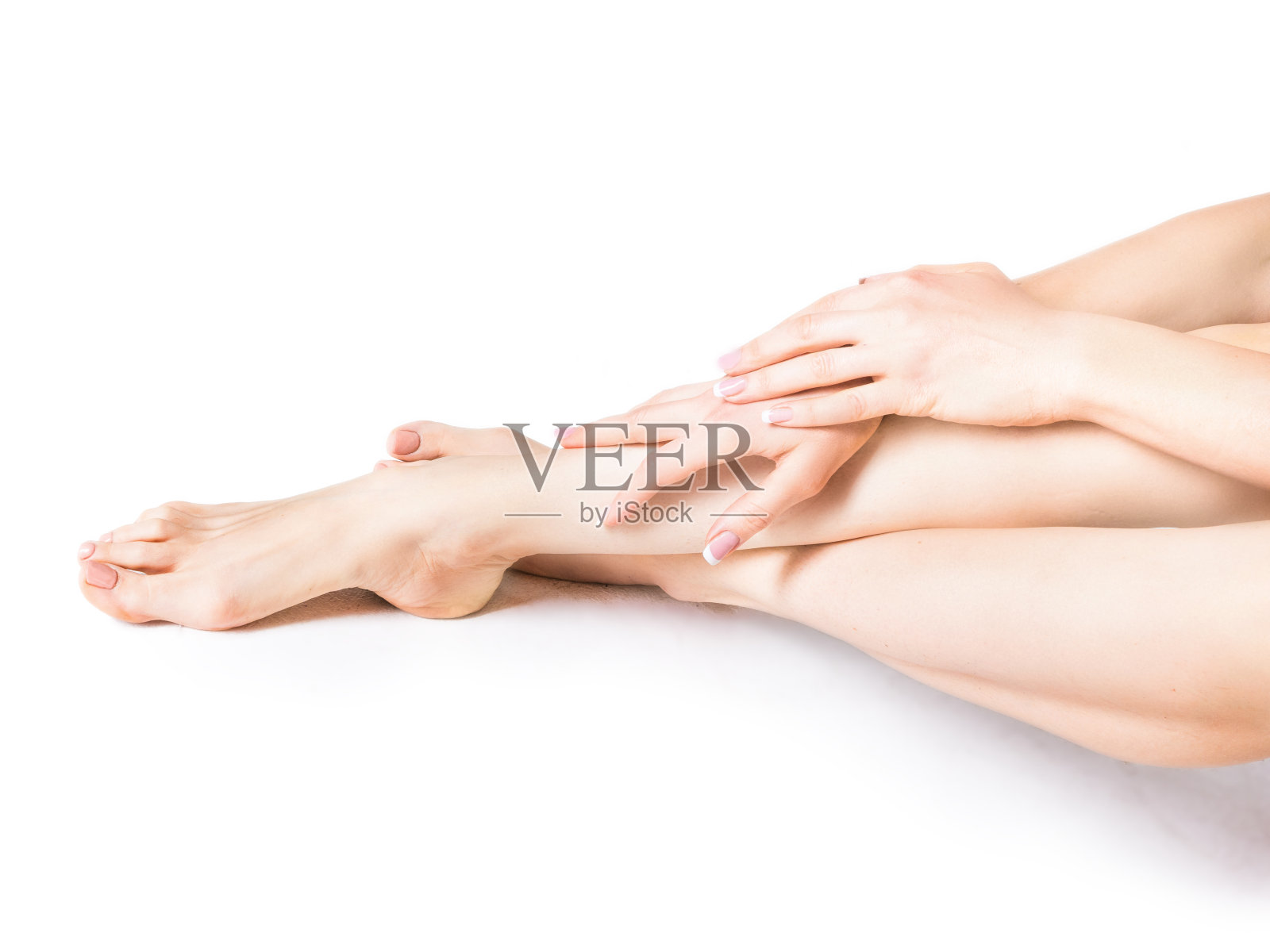 一个女人在她的腿和脚上涂抹保湿霜的特写镜头。美丽的脚和手孤立在白色的背景。年轻女子用法式美甲触摸着双手和双腿照片摄影图片