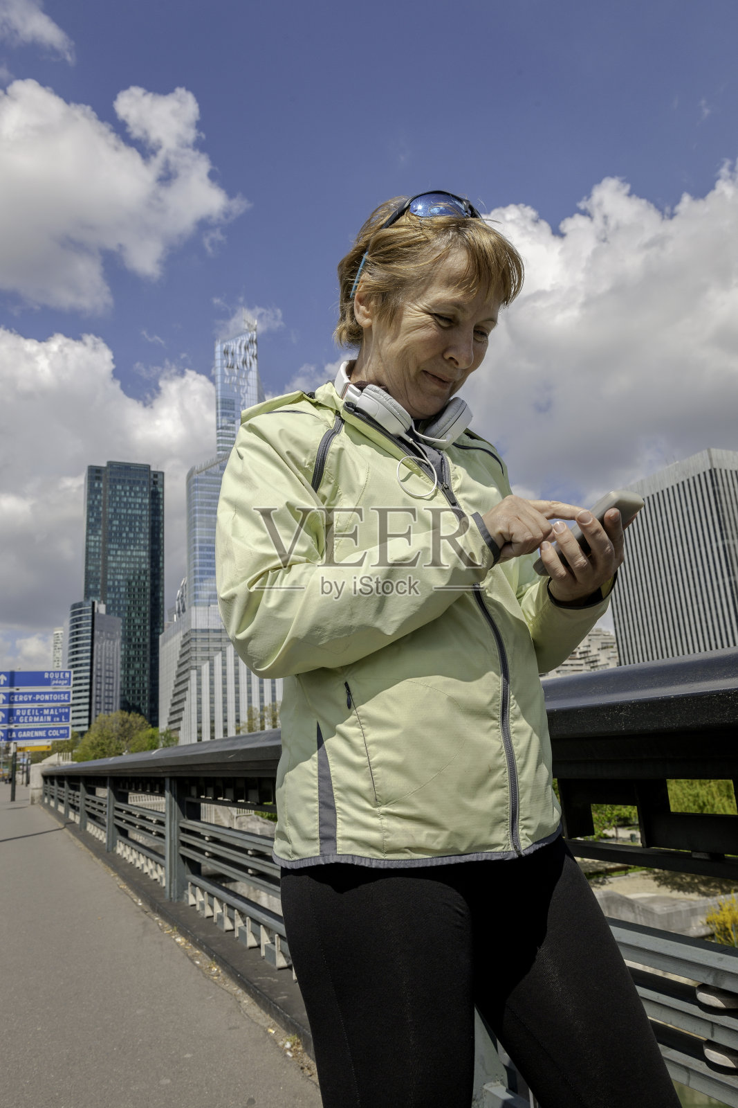 法国巴黎，塞纳河河畔的拉德芳斯，一个成熟的女人在跑步中使用手机照片摄影图片