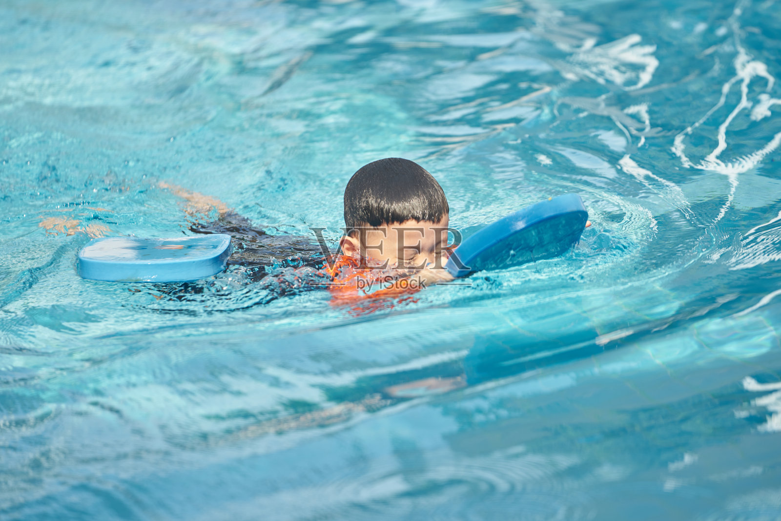 男孩在水中用泡沫垫练习游泳照片摄影图片