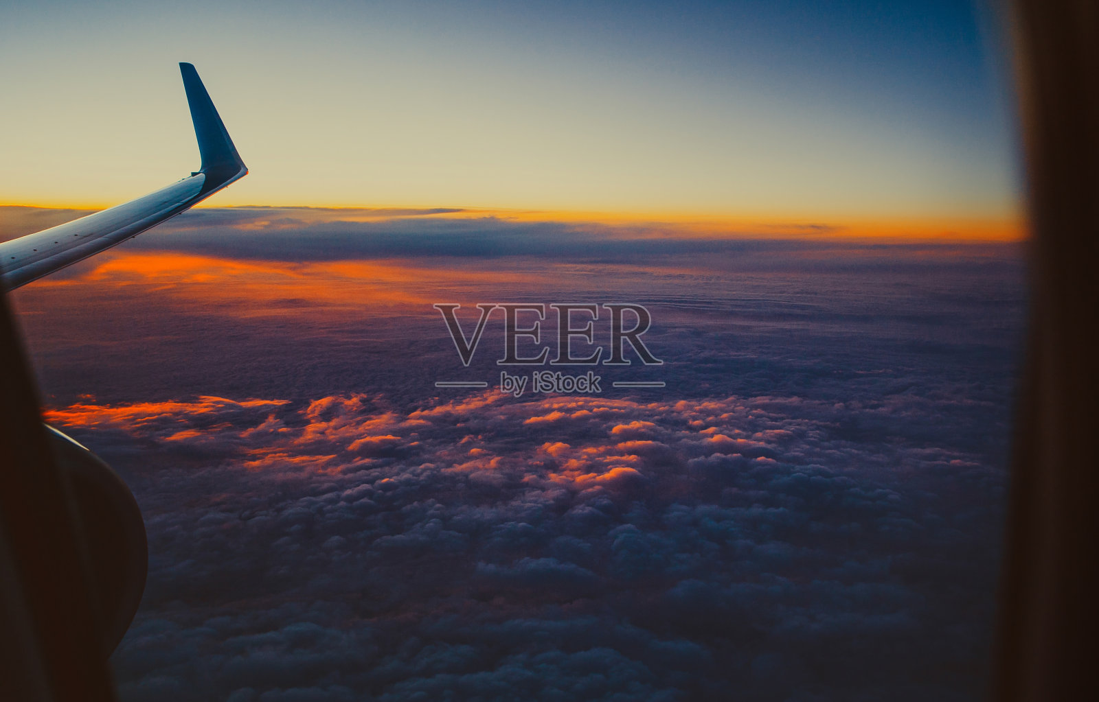 从舷窗可以看到美丽的景色。一架飞机的机翼在日落天空的背景与云突出在橙色。照片摄影图片