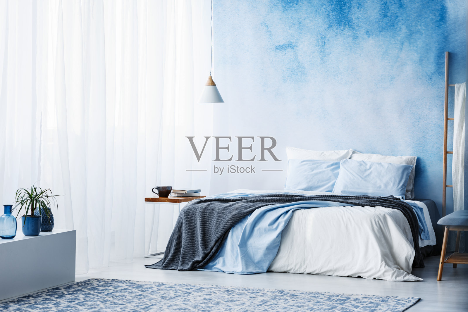 在宽敞的蓝色卧室内部白色的橱柜上种植植物，床上铺着灰色的毯子照片摄影图片