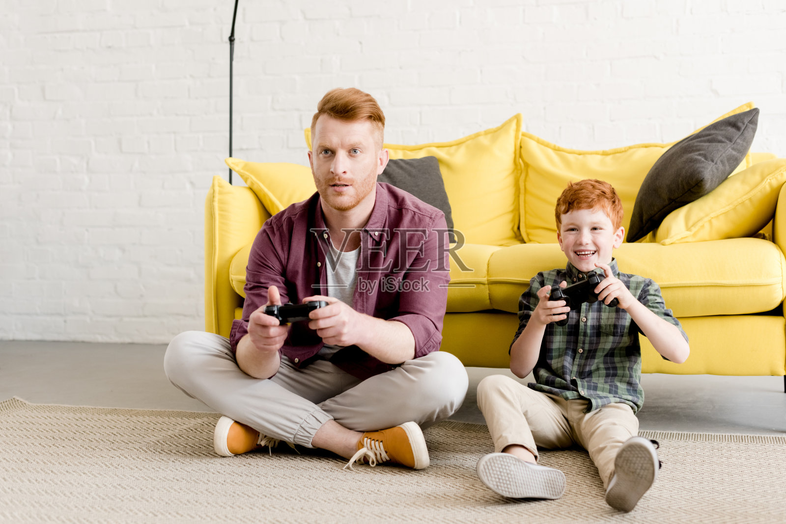快乐的父子俩坐在地毯上玩着家里的操纵杆照片摄影图片