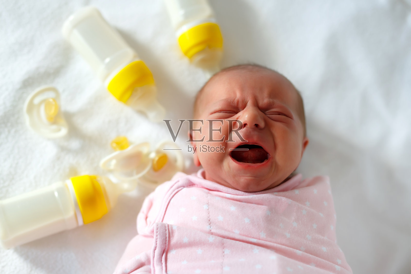 刚出生的女婴拿着奶瓶哭闹。婴儿配方饮料。照片摄影图片