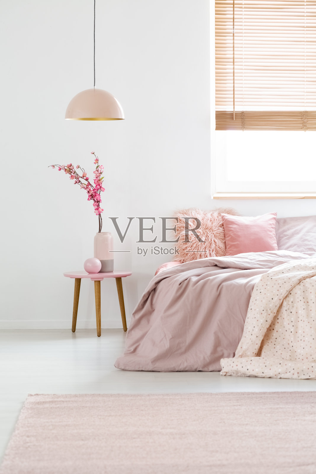 床头柜上的鲜花，桃红色的台灯和粉红色的床，在简单，柔和的卧室室内照片摄影图片