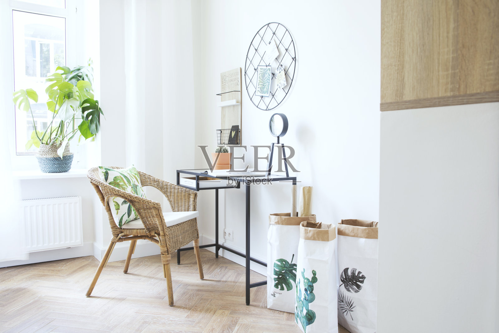 现代斯堪的纳维亚风格的室内家庭办公室配有玻璃桌子，设计时钟纸袋和植物。带有棕色木质拼花地板的时尚空间。照片摄影图片